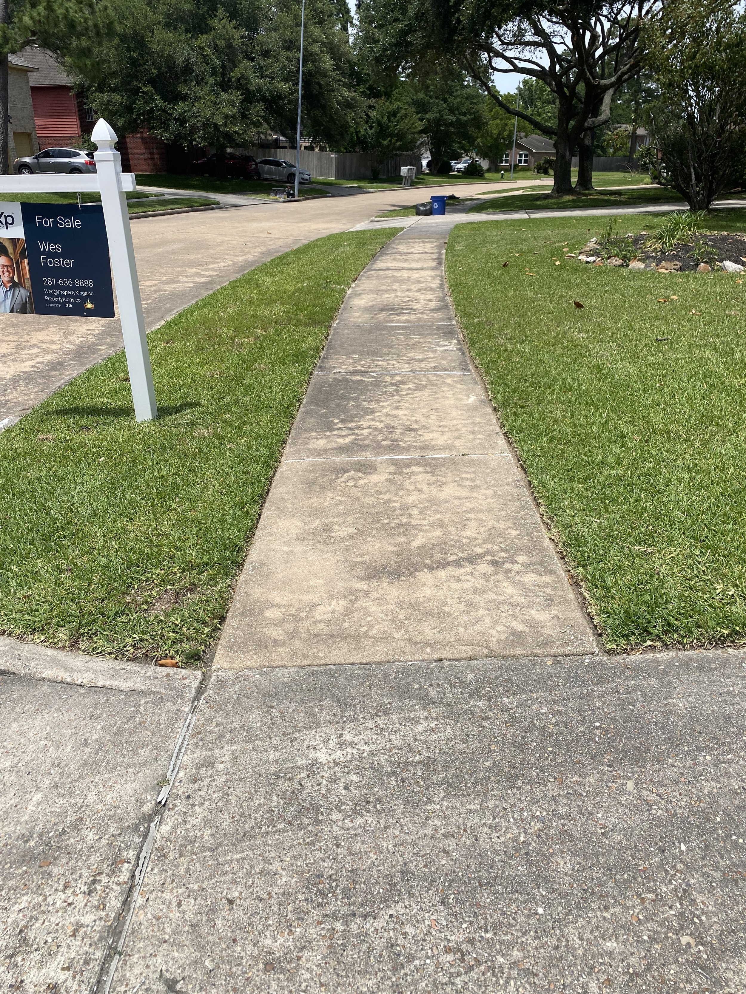 Curved neighborhood sidewalk in front of a home in Houston, TX, with visible grime, discoloration, and dark staining before pressure washing by Wyatt Washes