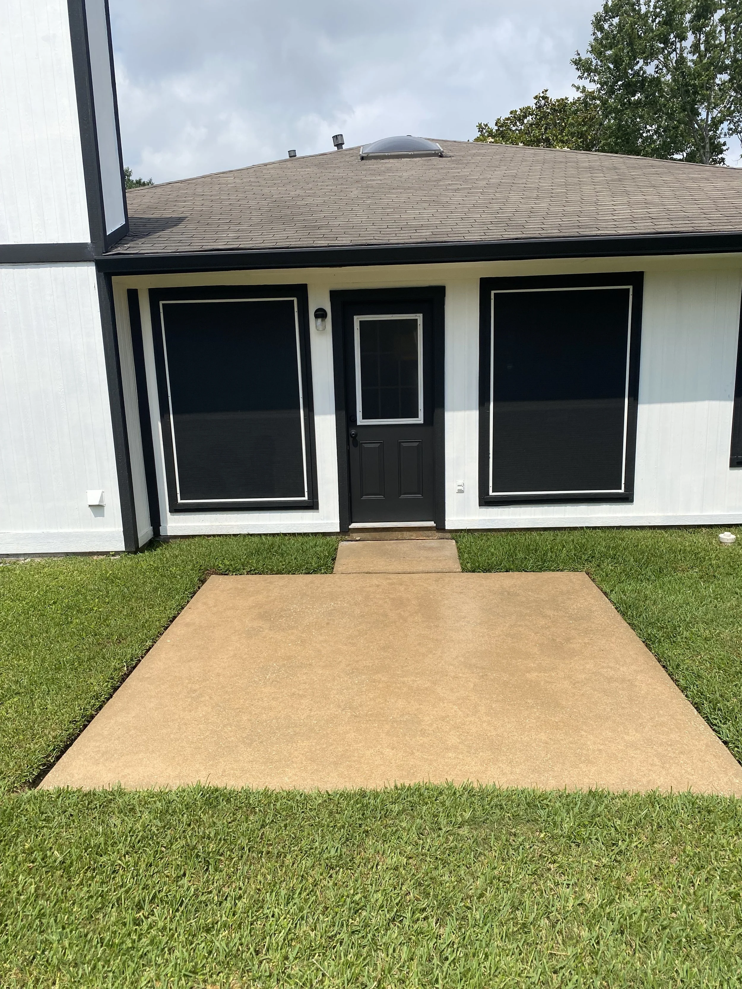"Clean and bright concrete patio after professional pressure washing by Wyatt Washes, showing refreshed surface in front of a white house with black trim in Houston, TX.