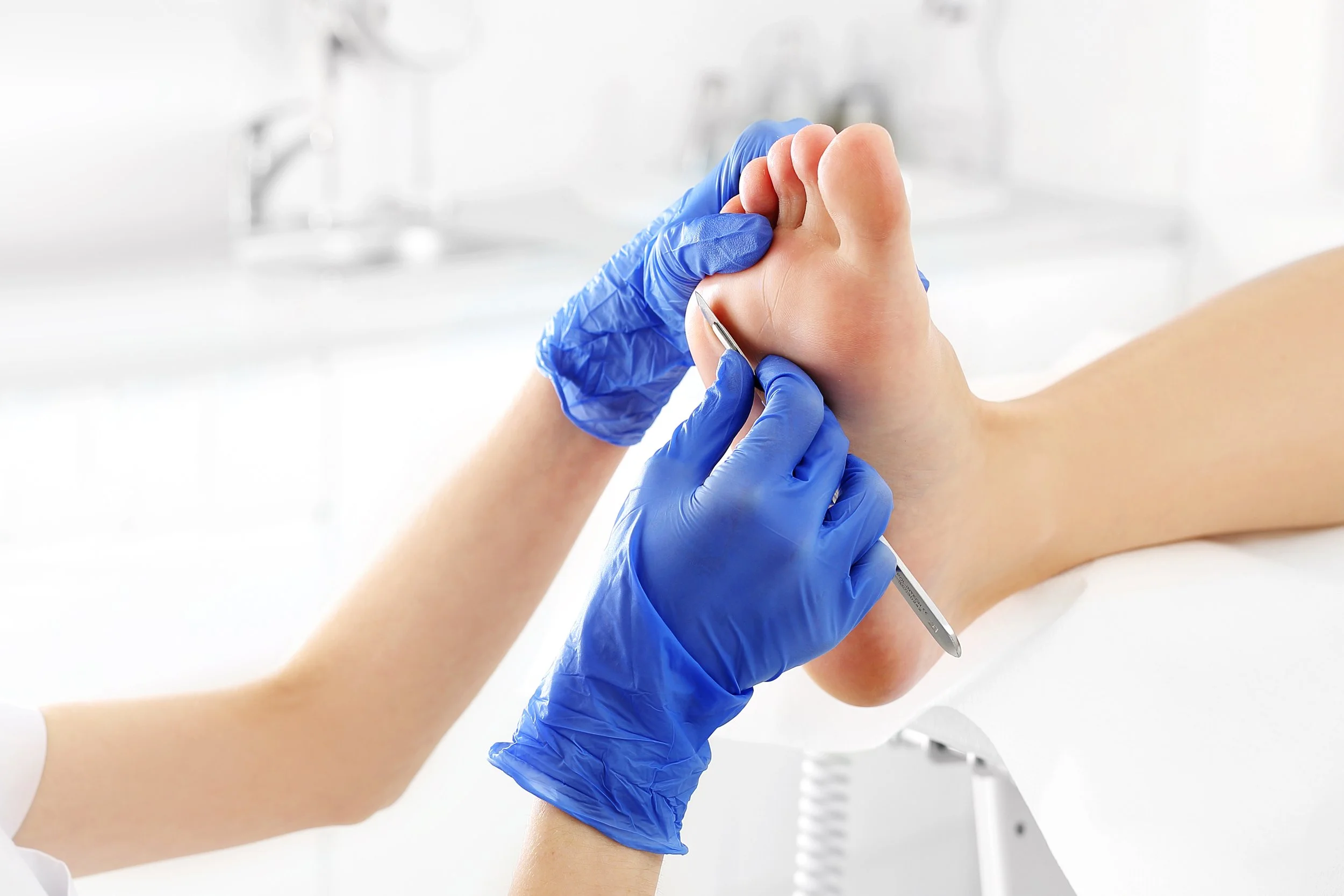 Podiatrist performing foot care on patient's foot with blue gloves and medical tool in a clinic.