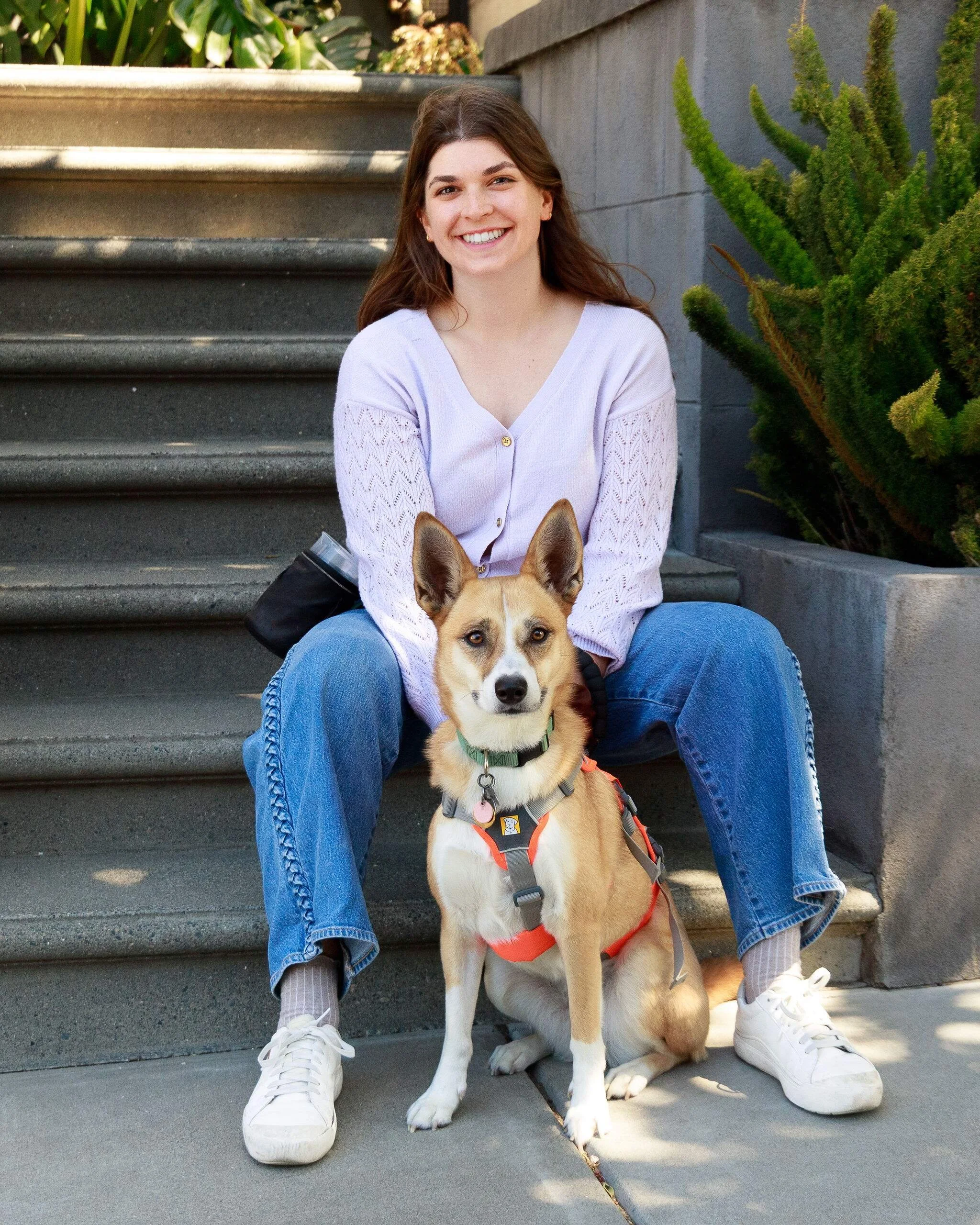 Young woman sits on stairs with her dog seated in front of and below her between her bent legs.