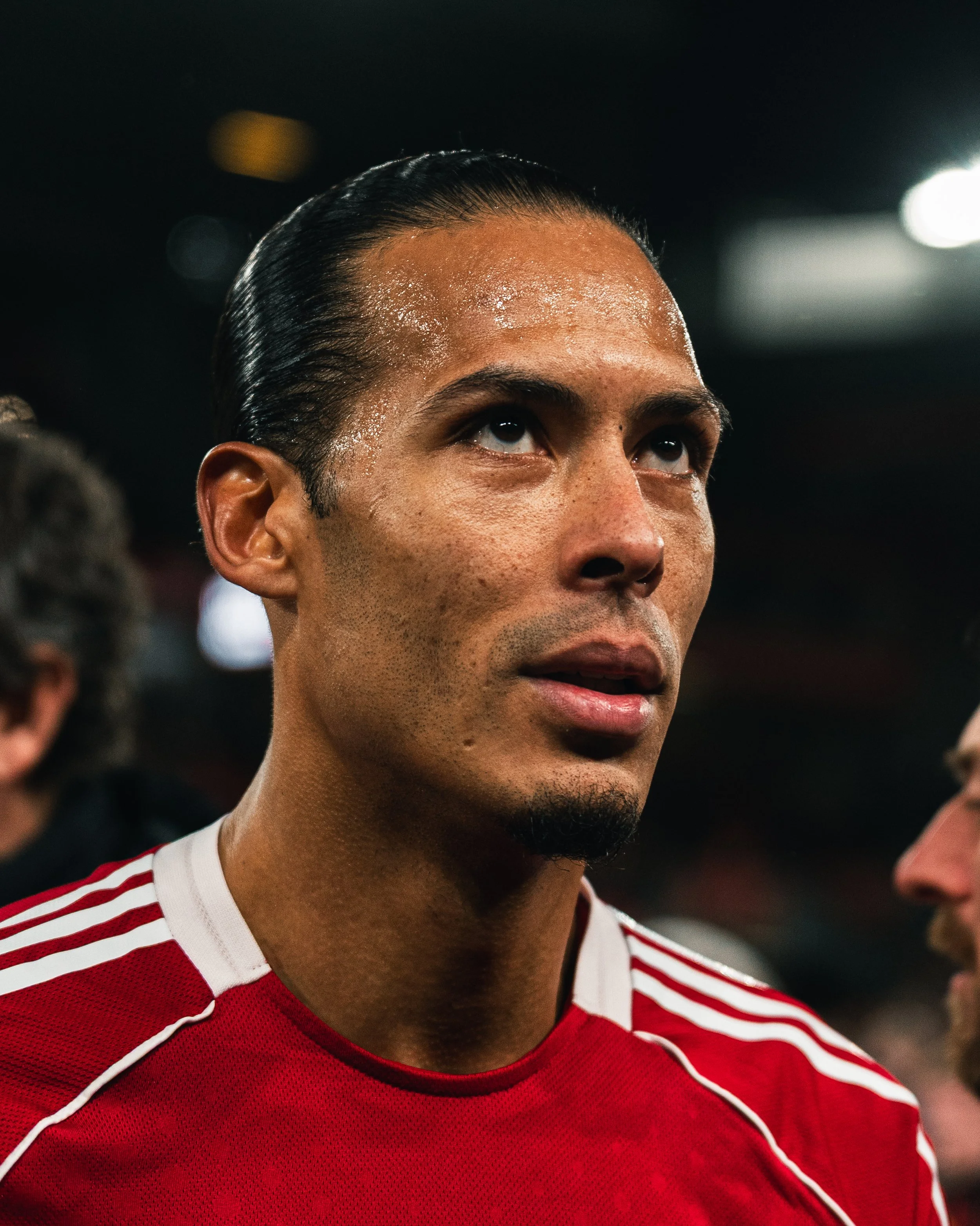 Un homme avec les cheveux noirs, parés d'une transpiration, portant un maillot rouge, regarde vers le haut.