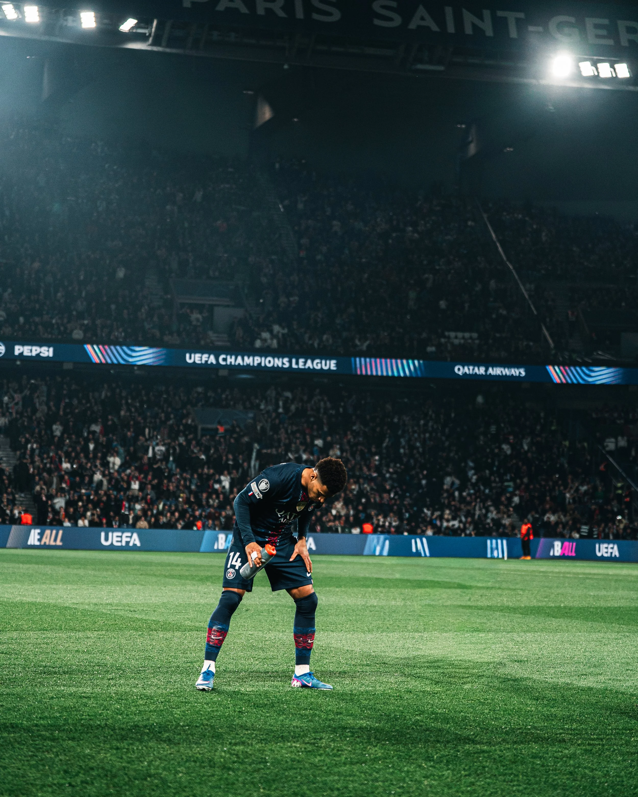 Un joueur de football du Paris Saint-Germain se baisse sur le terrain à la fin d'un match européen, avec un stade rempli en arrière-plan.