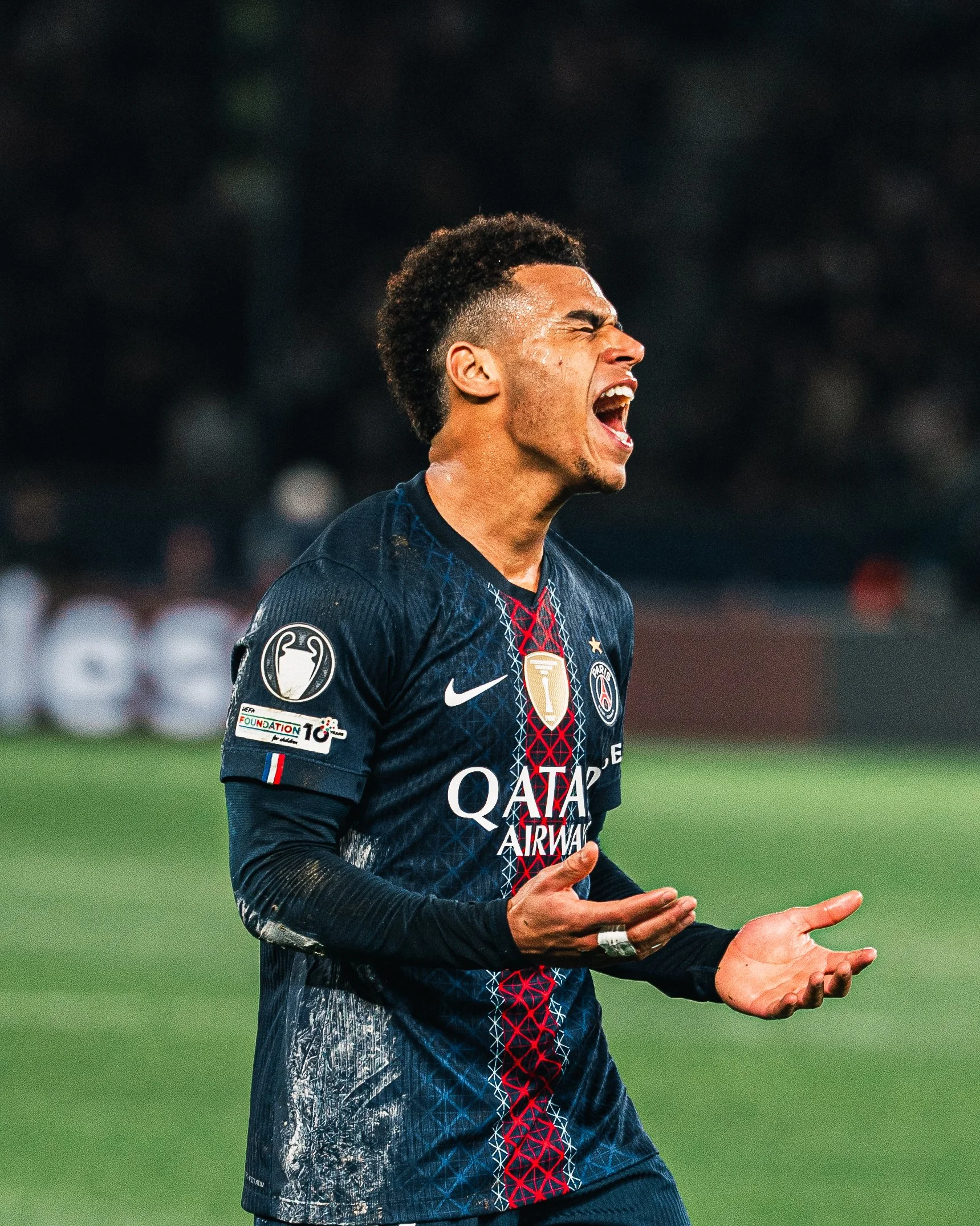 Un footballeur en action, portant le maillot du Paris Saint-Germain, en plein match, avec une expression de joie intense, montrant son émotion sur le terrain.