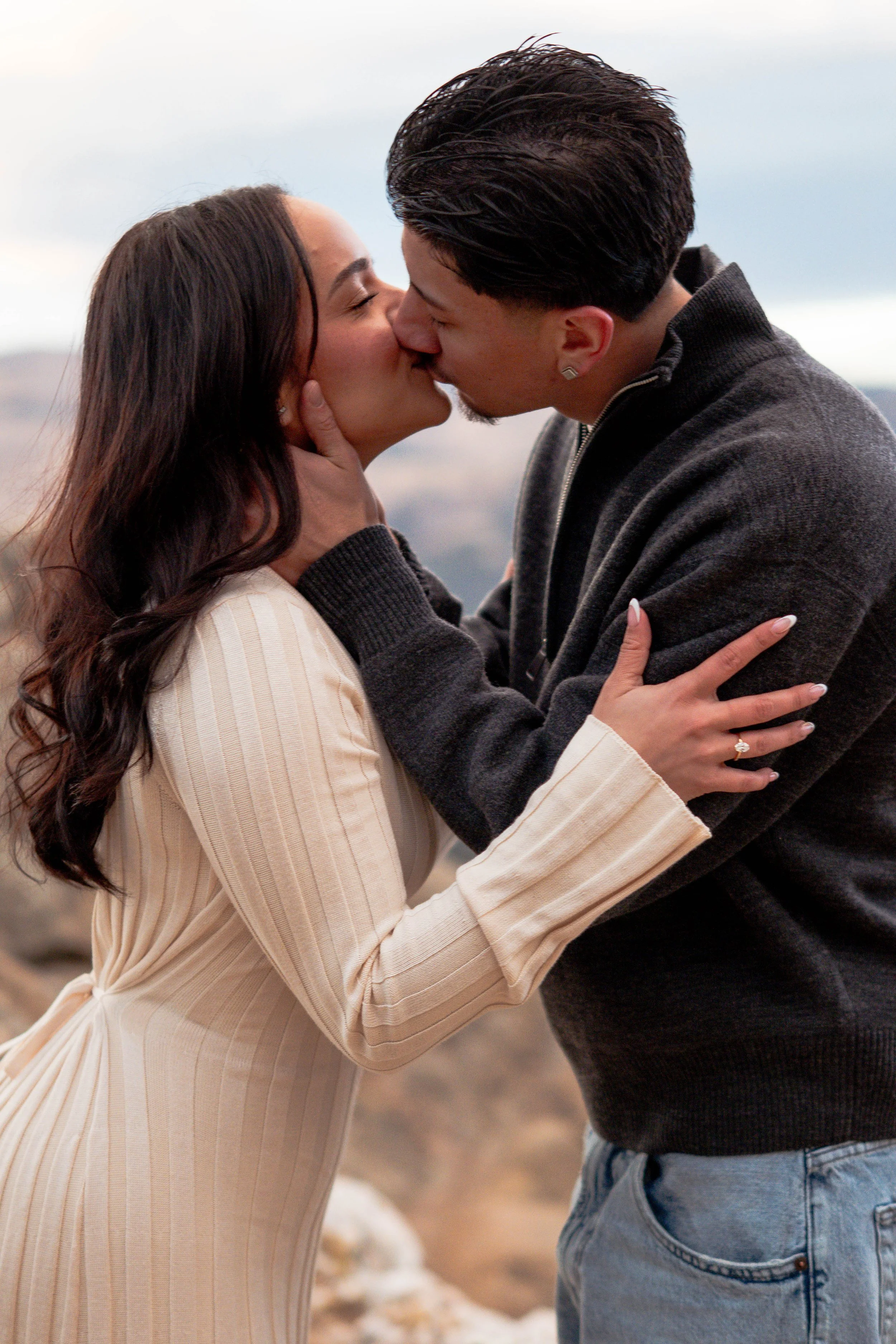 A couple sharing a passionate kiss outdoors with a rocky landscape in the background.