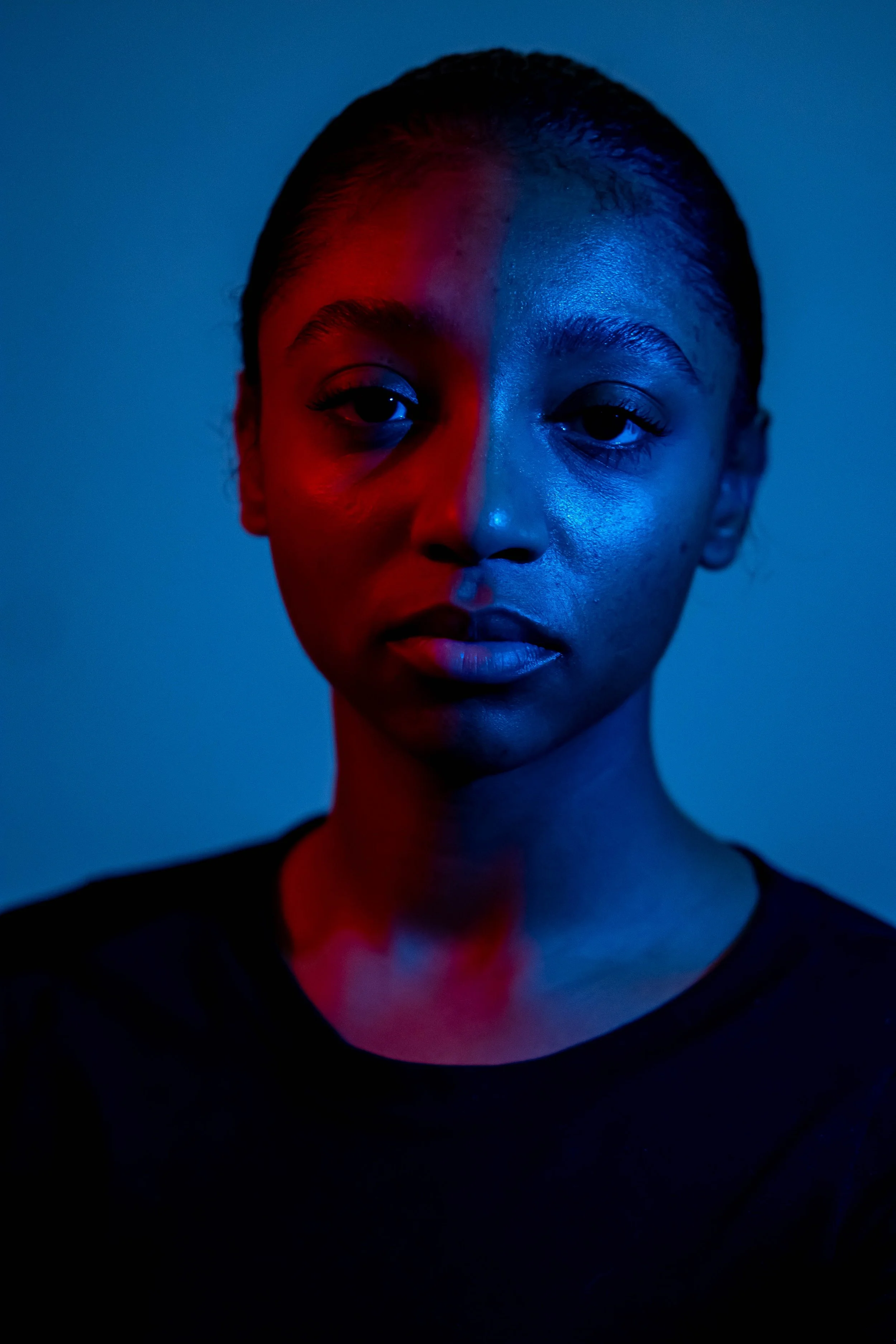 A portrait of a young woman with short hair, illuminated with red and blue lighting.