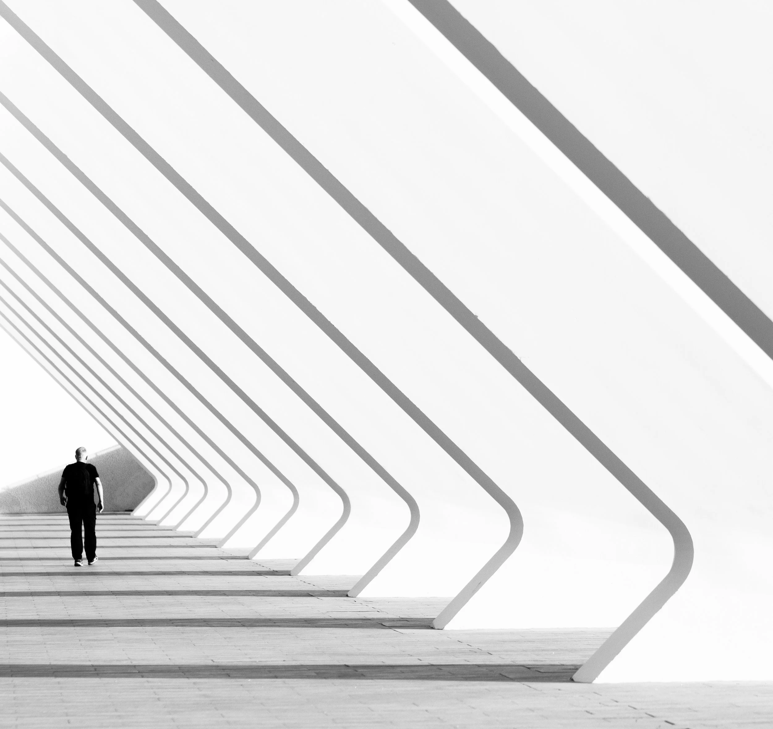 A person walking alone under a modern architectural structure with repetitive geometric shapes in black and white.