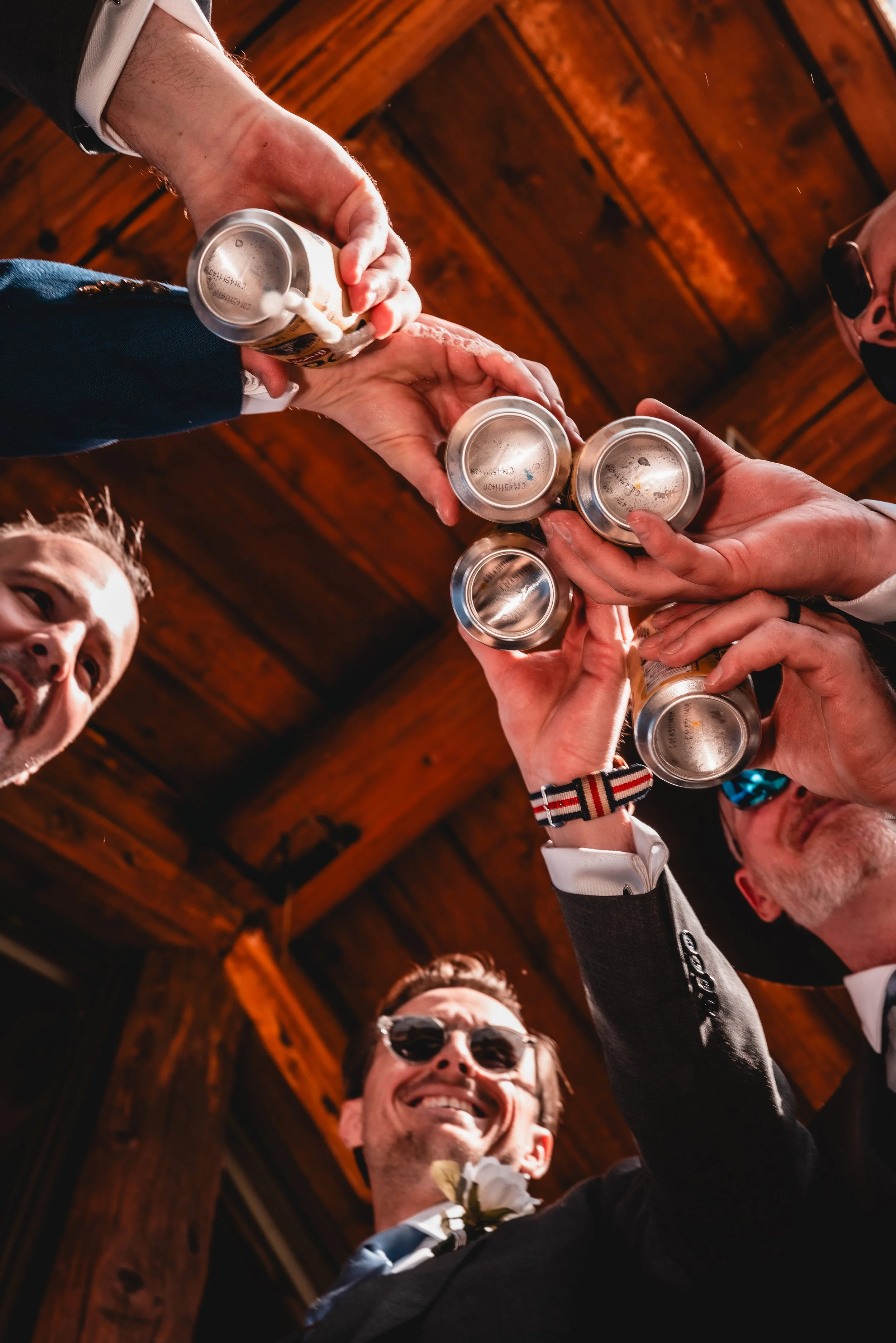 Group of people toasting with metal cans at a celebration in a wooden setting.