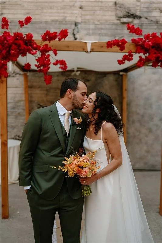 Bride and Groom kiss under their red floral adorned wood beam alter at the Ice House Wedding Venue. 
Photography By: Andrea Cakmar Photo + Film