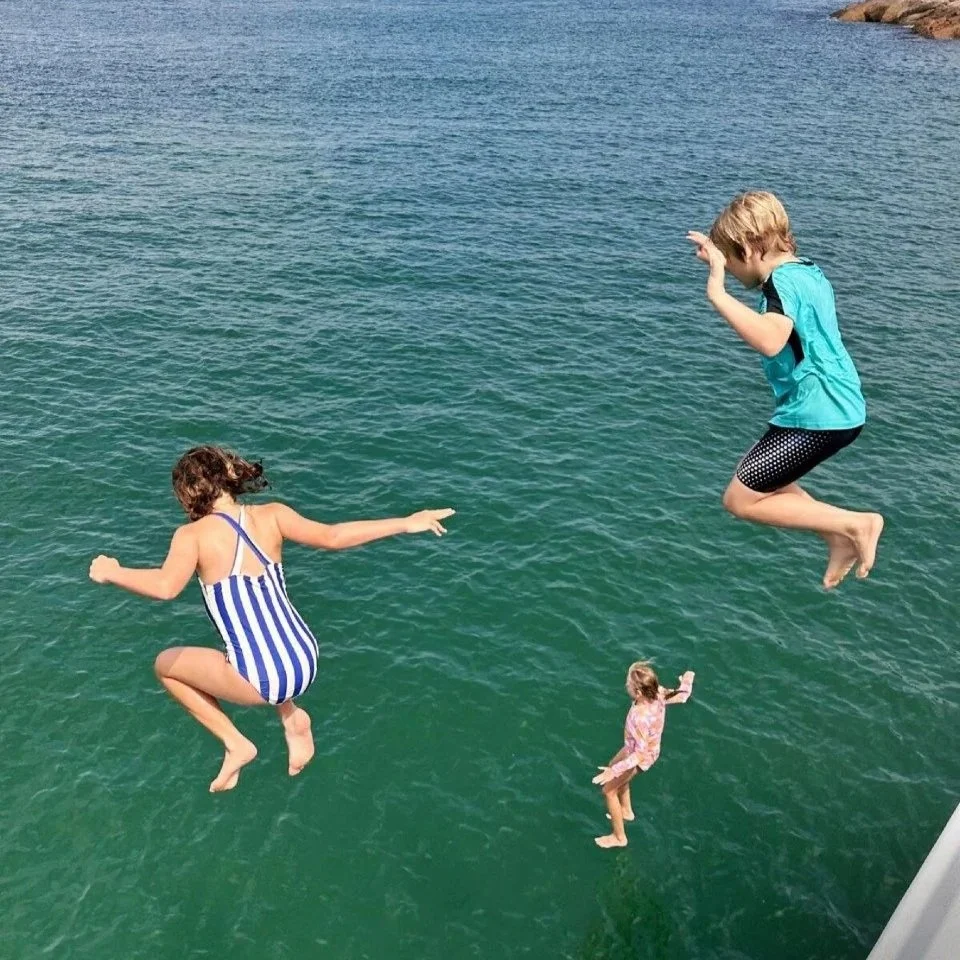 Three children jumping off the side of a junk boat into the deep blue ocean during a family-friendly charter.