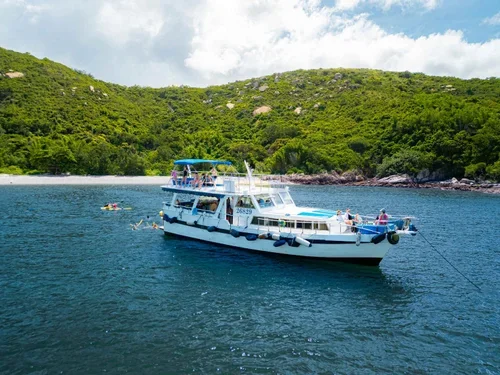 A white boat anchored in a body of water with a lush, green hillside in the background.