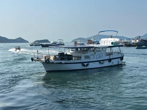 A white boat with blue accents sailing on the water with boats and islands in the background.