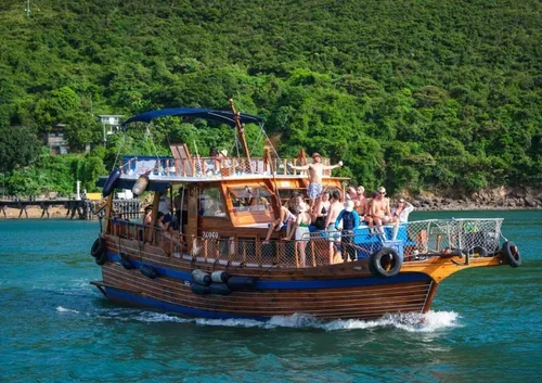A boat with people on board sailing on turquoise water near a green, forested shoreline.