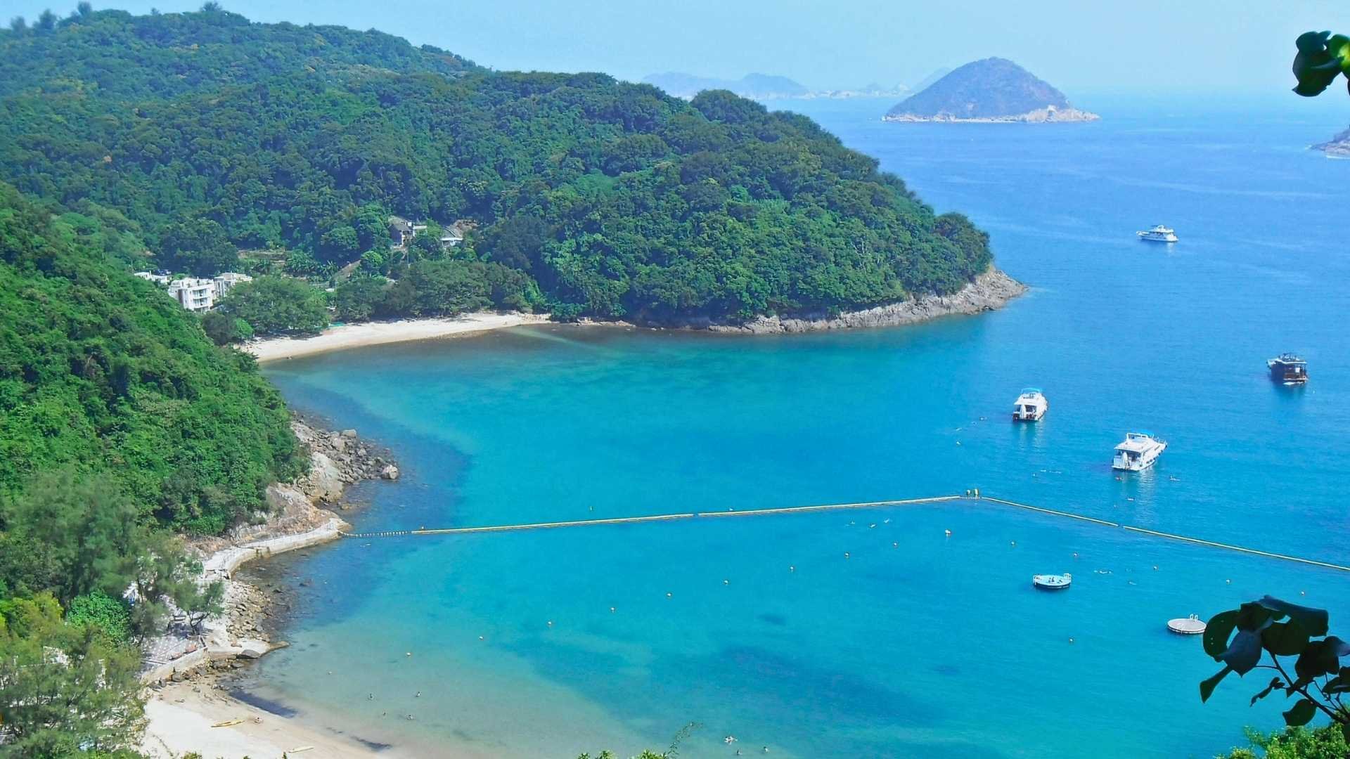 A traditional junk boat anchored in the turquoise waters of Clearwater Bay, Hong Kong, surrounded by lush green hills.