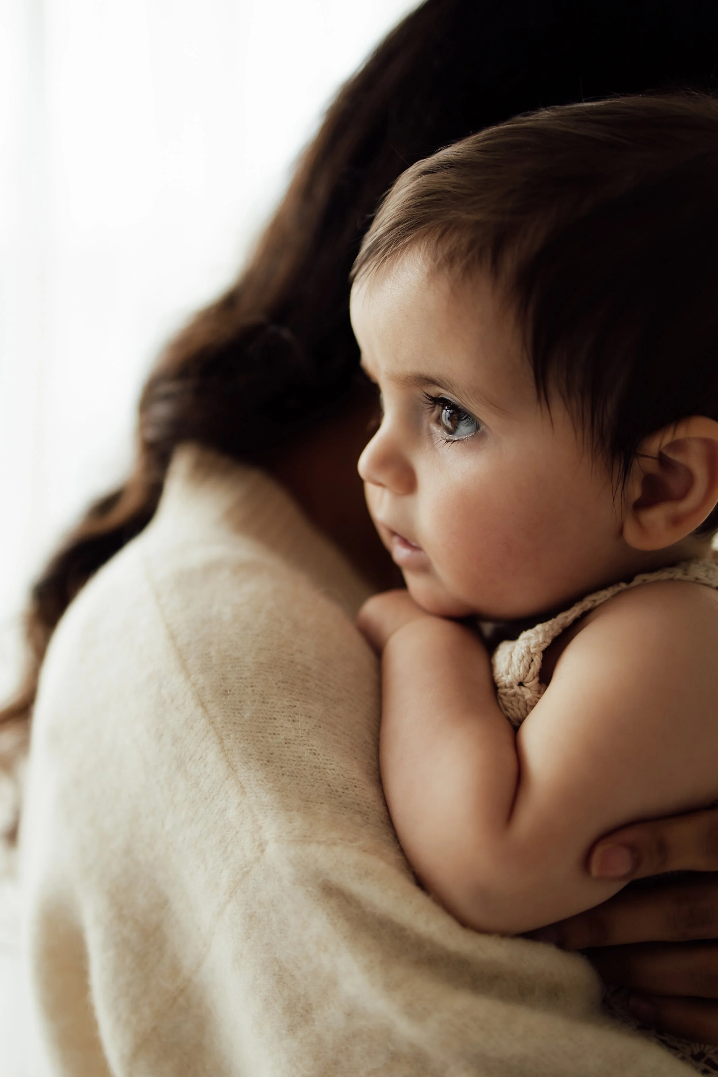 Baby looks over mum's shoulder while she cuddles her