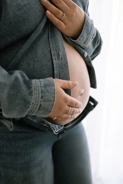Expectant mum wearing a denim shirt, which is unbuttoned to show her bump, resting her hand on her baby bump
