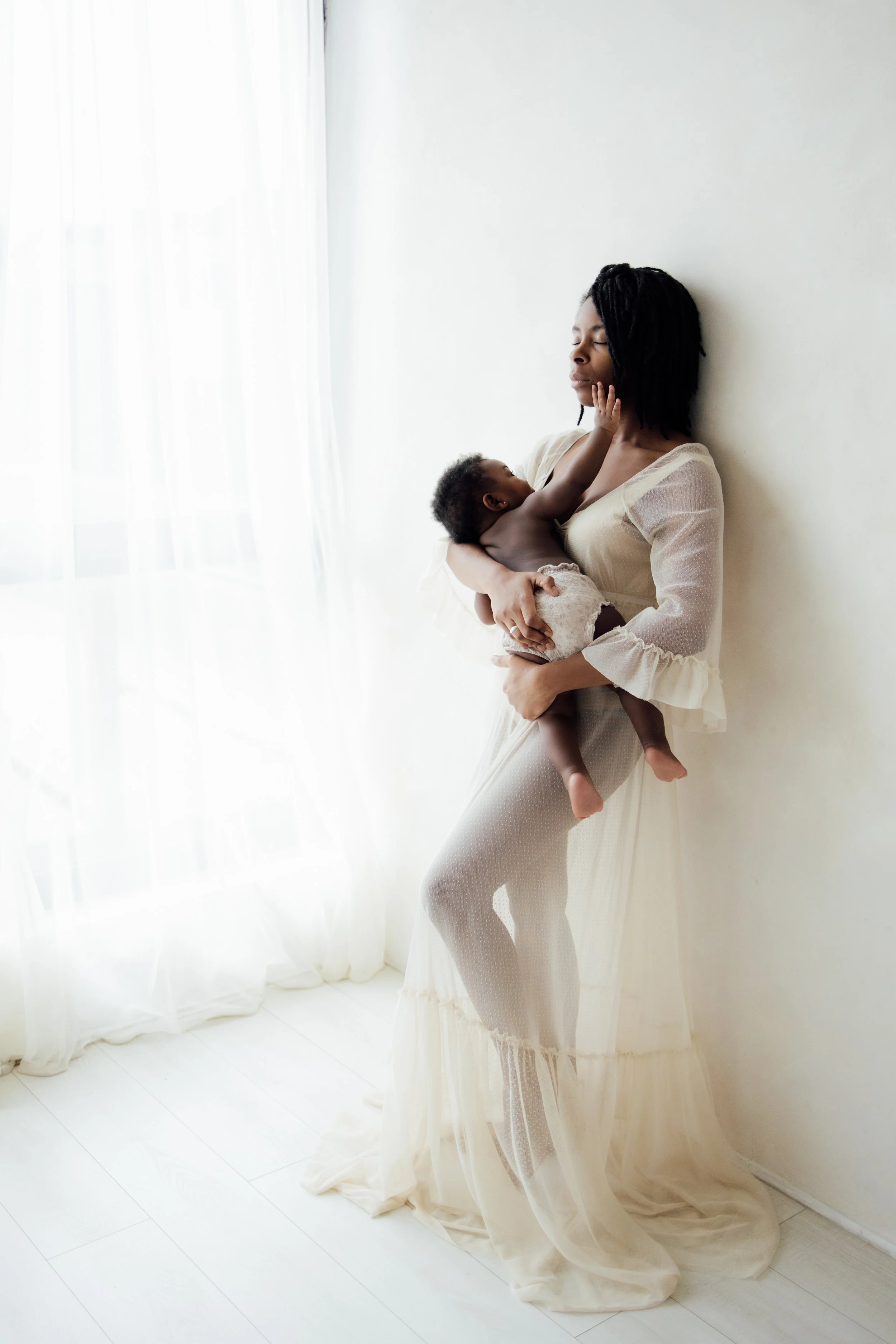 Mother stands and rests against wall while feeding her baby