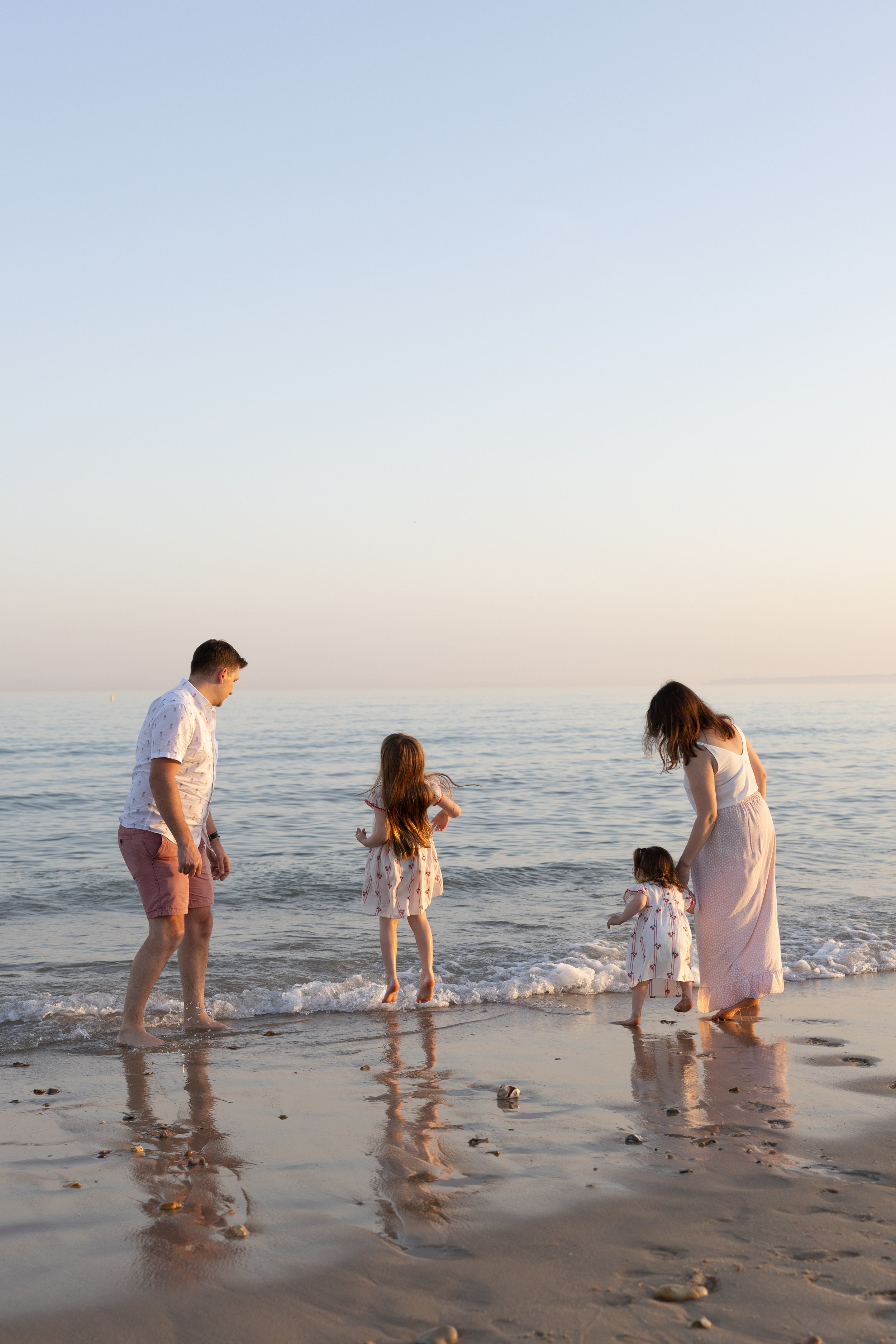 Family of four play in the shallows on the beach at golden hour during a family photoshoot