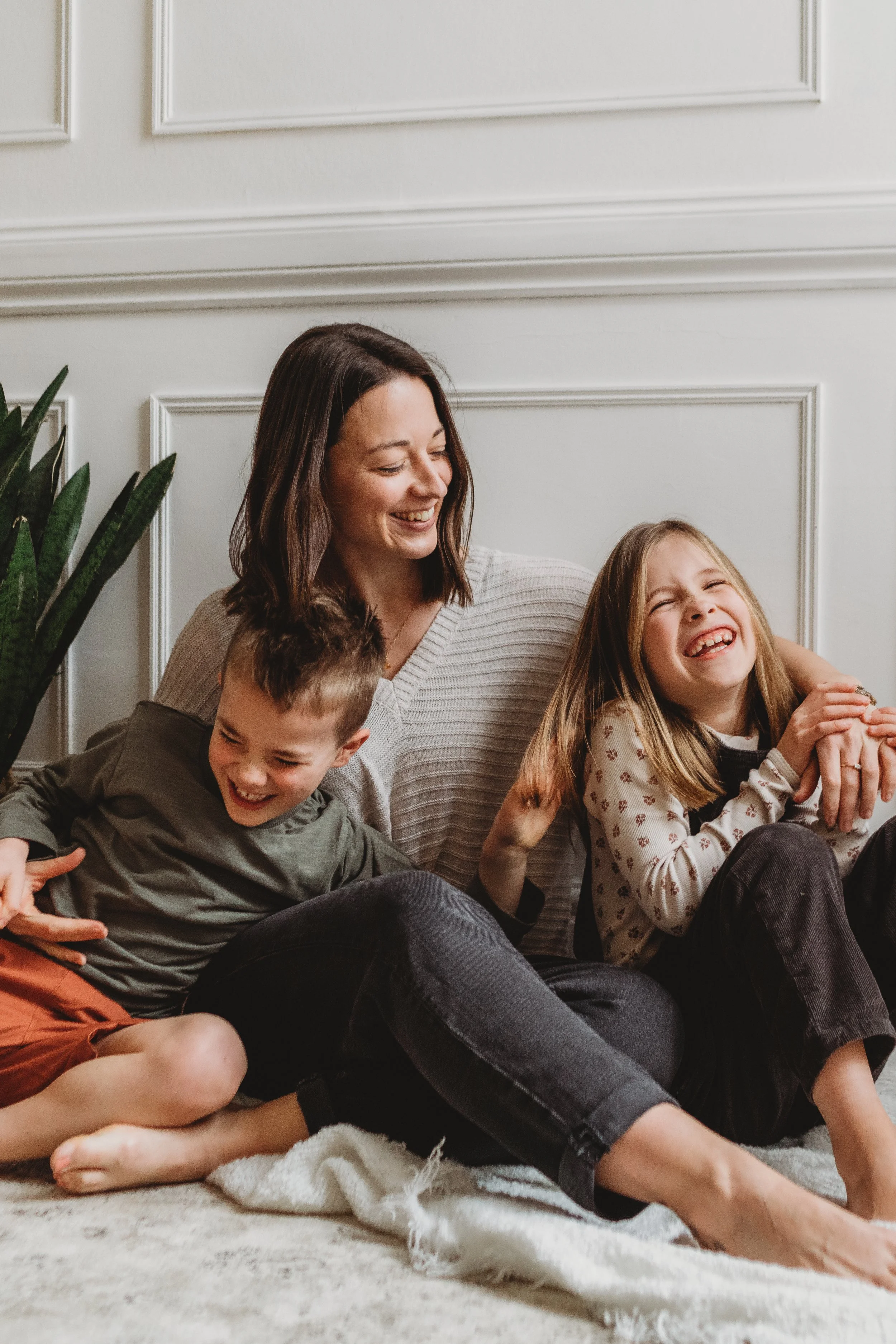A mother and her two children sit on the floor, cuddling and laughing together