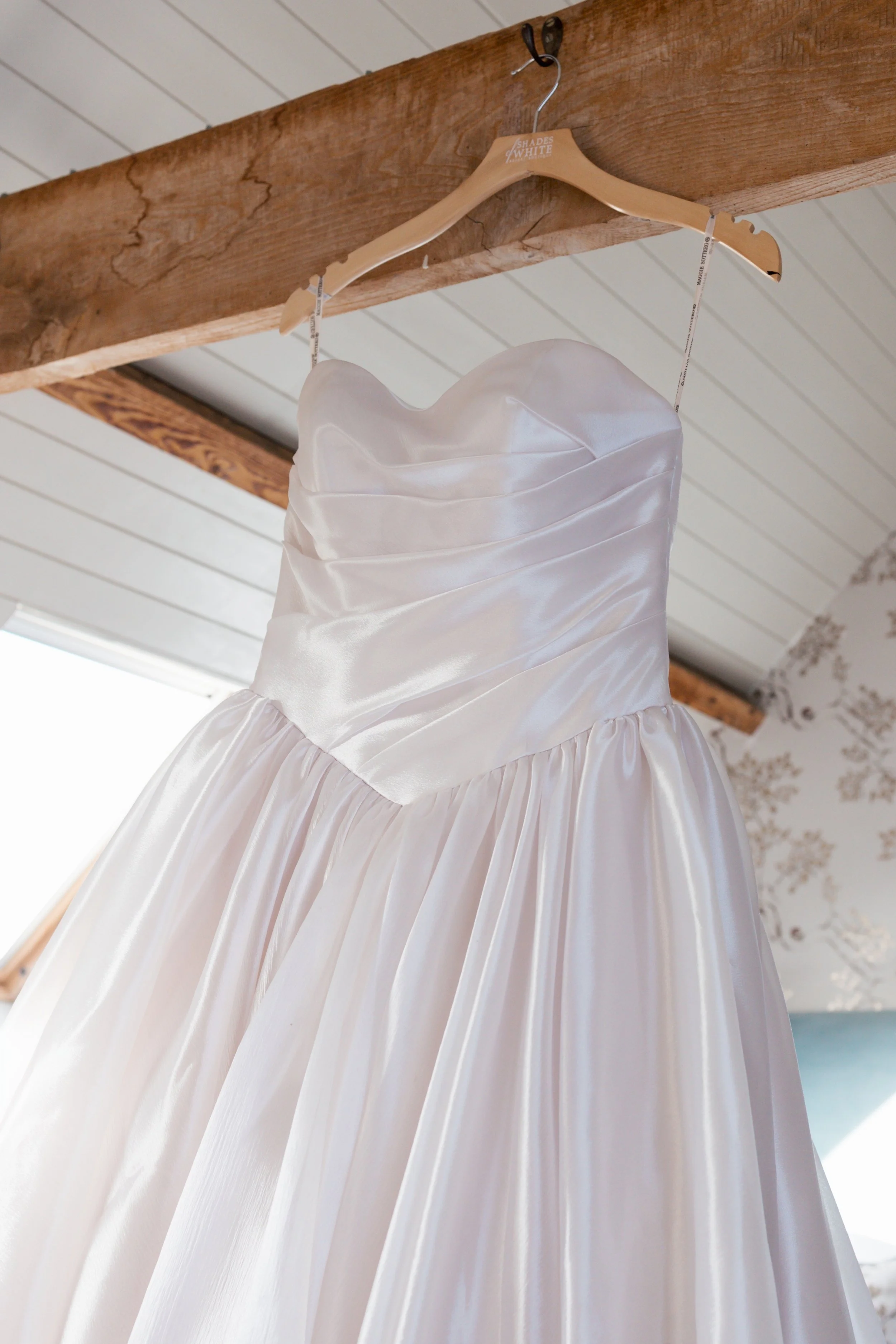 White satin wedding dress hangs in bedroom on morning of wedding