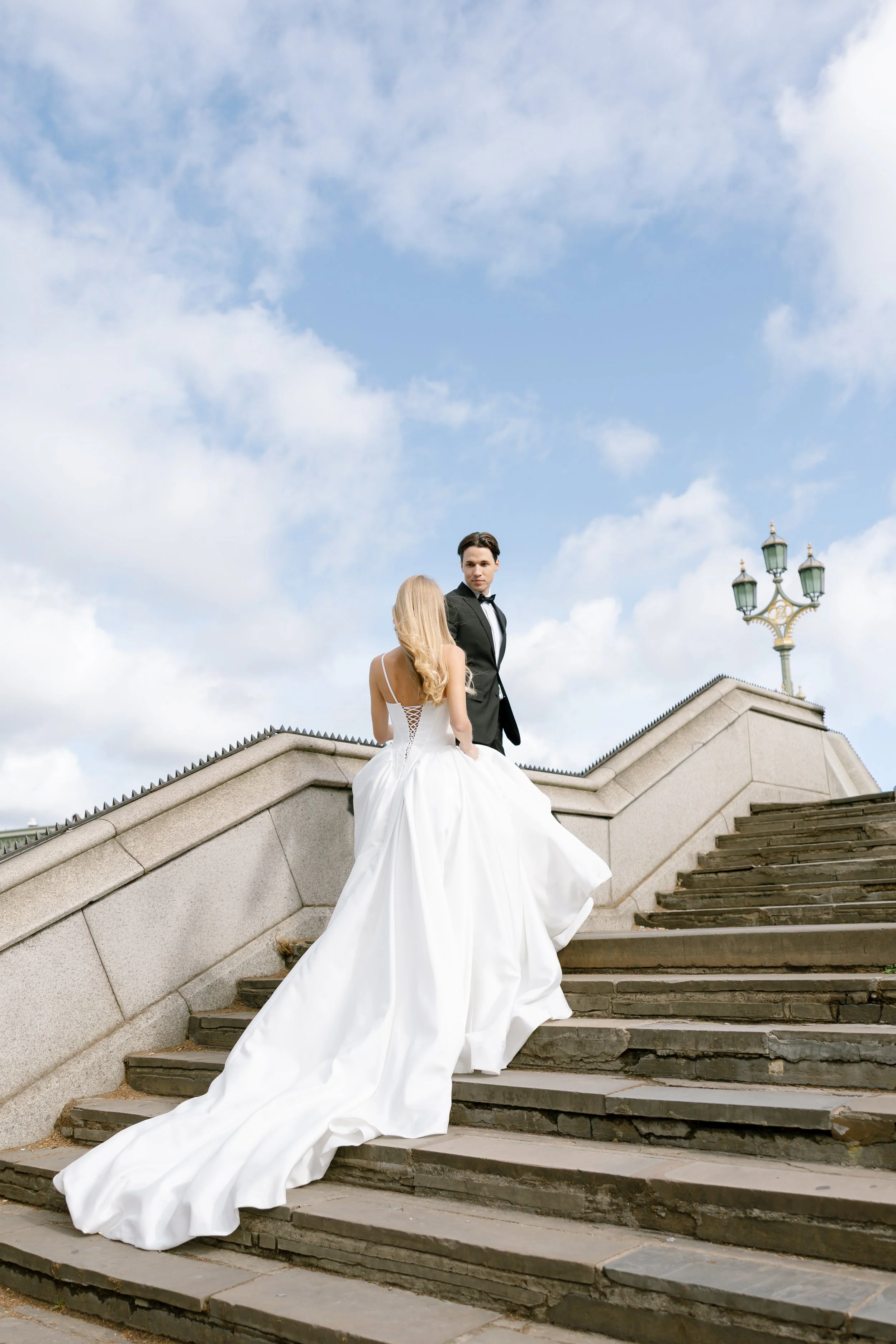 Bride dressed in elegant dress walks up steps of London Bridge with groom