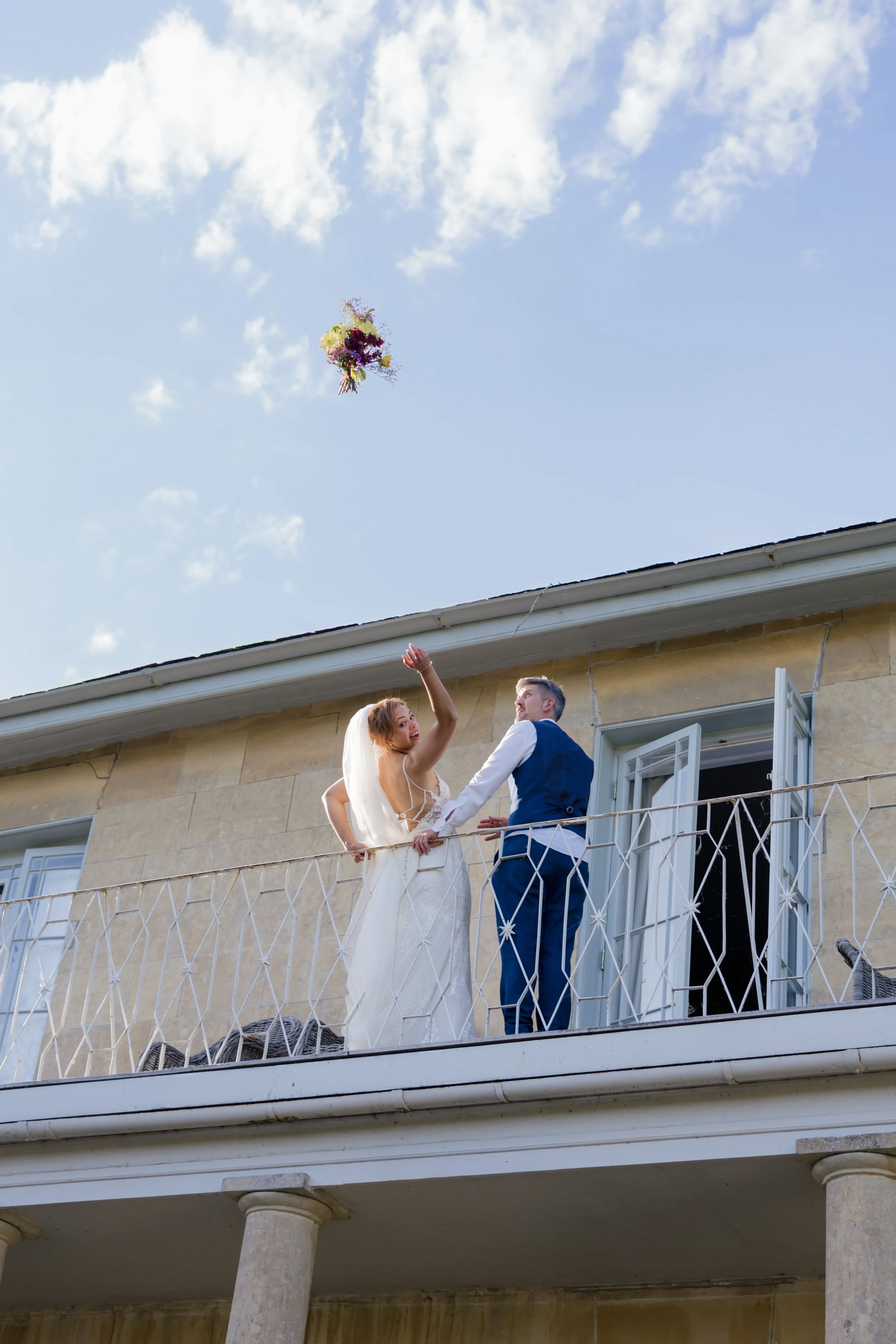 Bride and groom stand on balcony at Henge Estate and bride throws her bouquet to assembled guests who are out of shot
