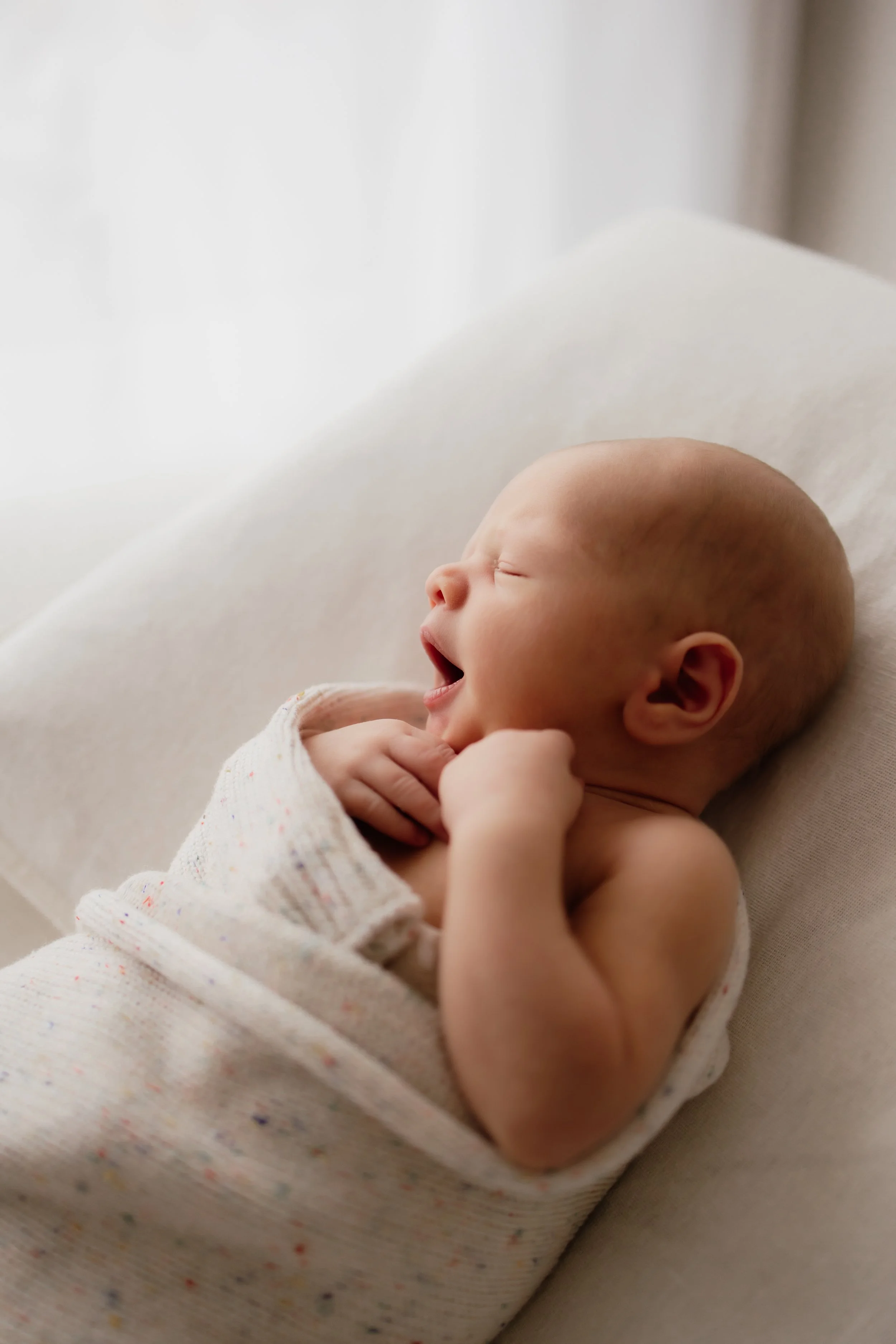 Newborn wrapped up in a blanket yawning widely