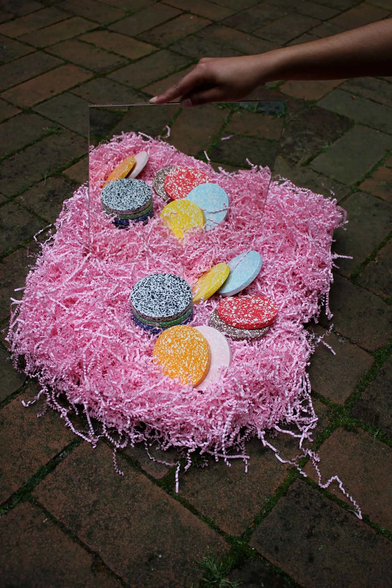 Künstlerische Inszenierung: Ein Bett aus rosa Papierschnipseln präsentiert verschiedene Terrazzo-Untersetzer mit weißen Terrazzochips auf kräftigen Grundfarben.
