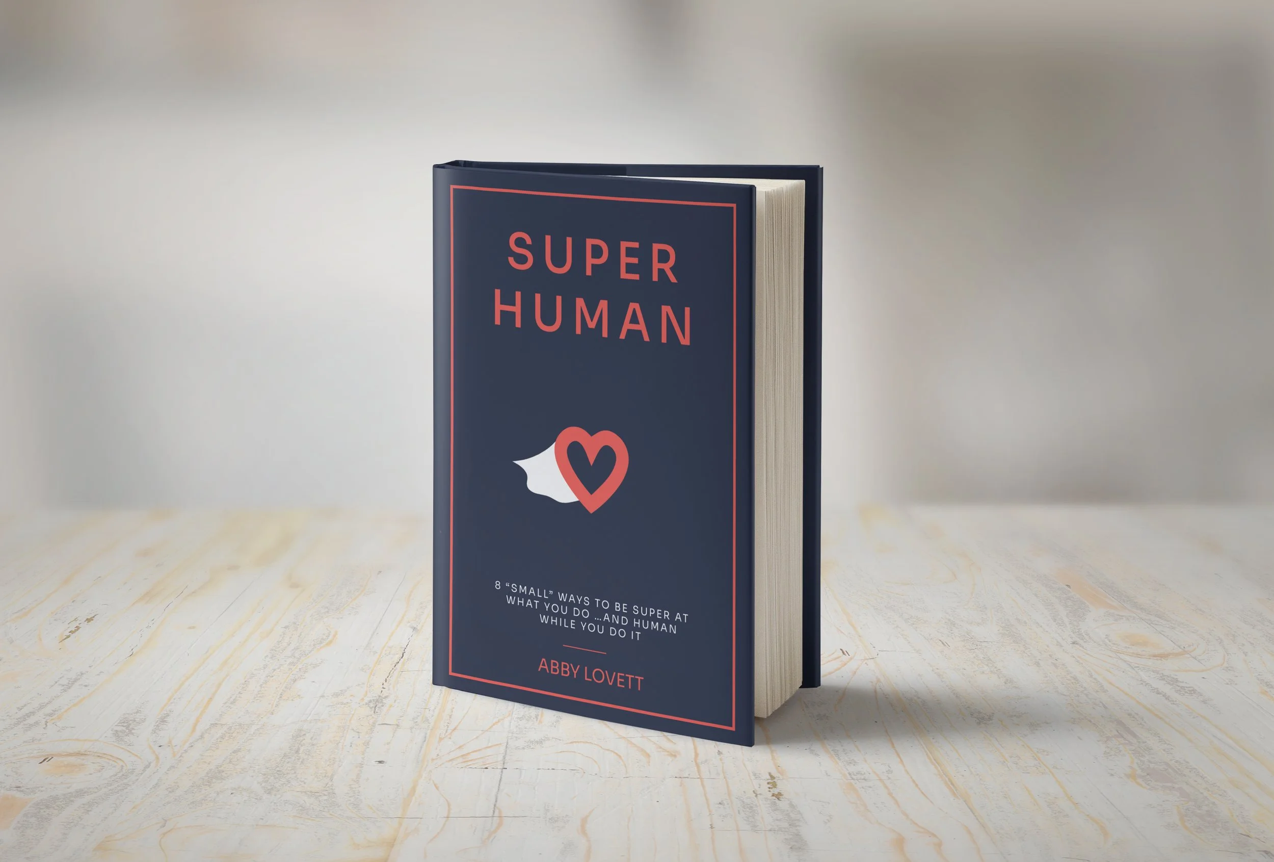 A book titled 'Super Human' by Abby Lovett standing upright on a light wooden surface. The book cover is dark blue with red and white text and heart-shaped graphics.