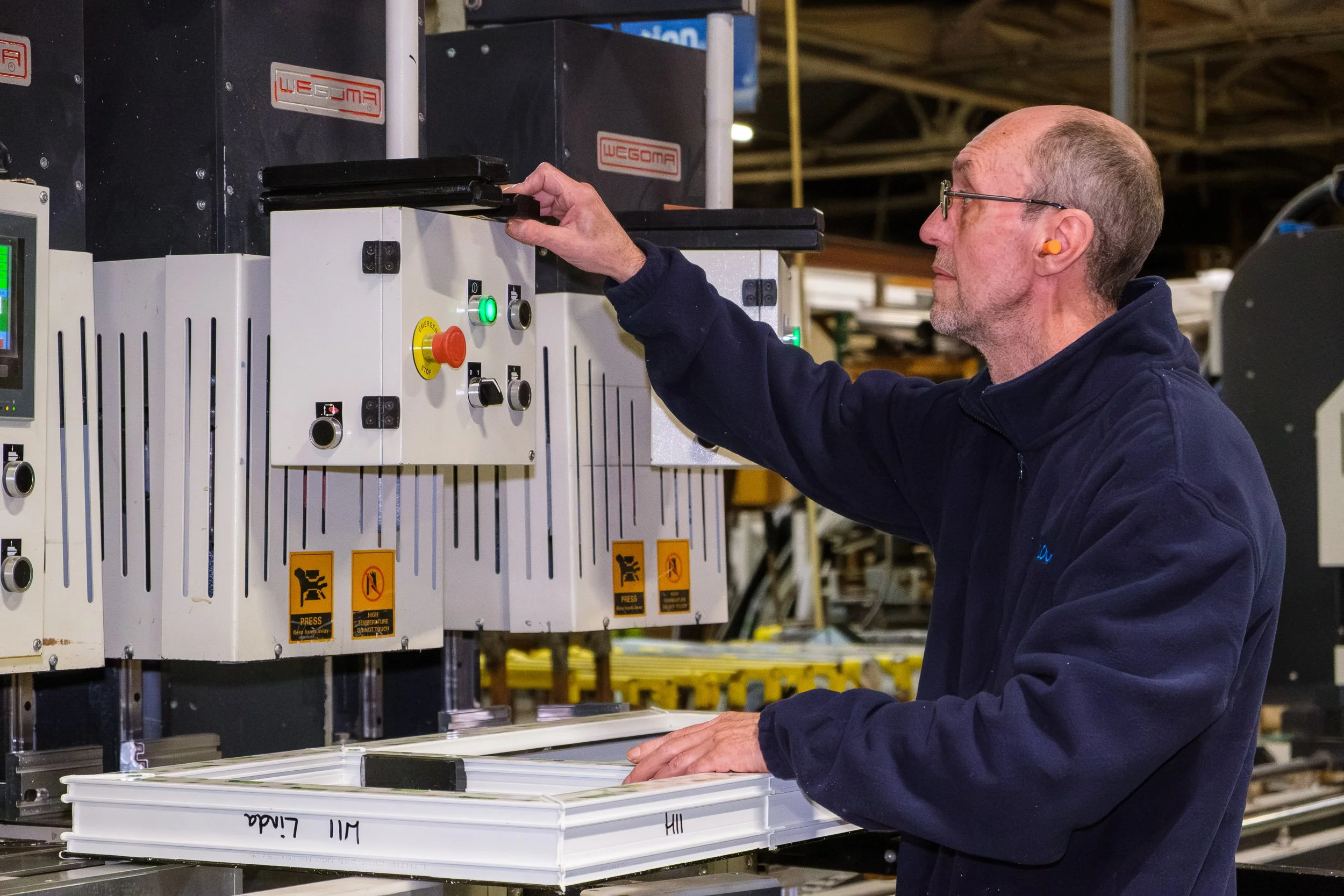A man wearing safety glasses and earplugs operating a machine in a factory or workshop.