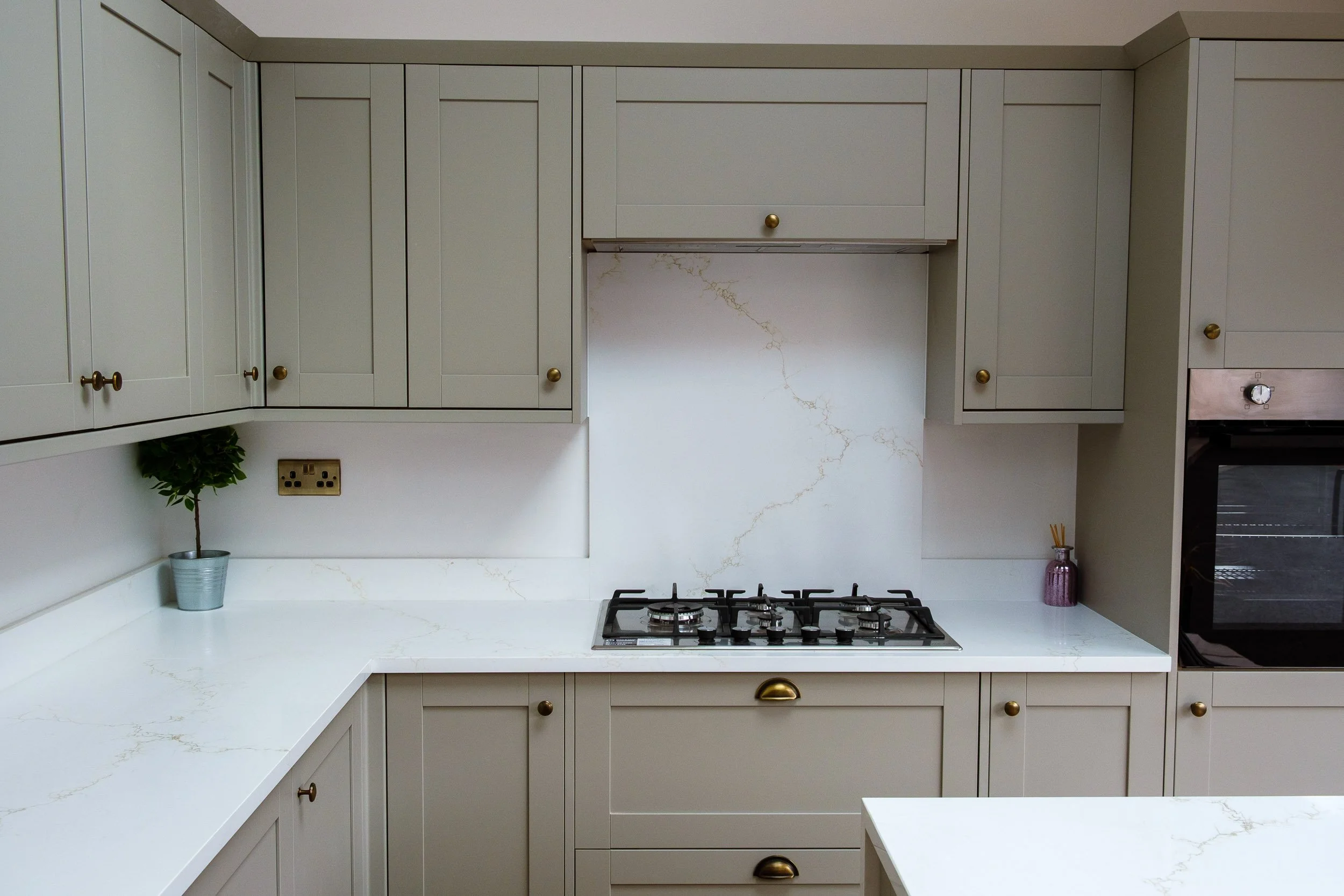 Modern kitchen with cream-colored cabinets, marble countertops, and a gas stove, featuring a small potted plant and a purple vase with sticks.