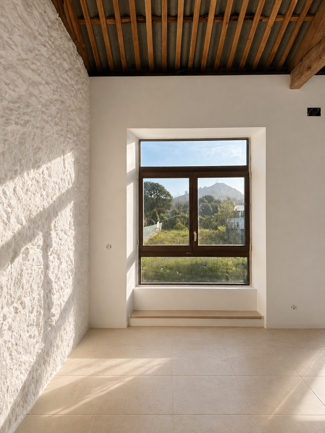 Detalle de iluminación natural en la rehabilitación de la Escuela Unitaria de San Lorenzo en A Guarda (Galicia), destacando el diálogo entre carpintería de madera y muros de piedra existentes.