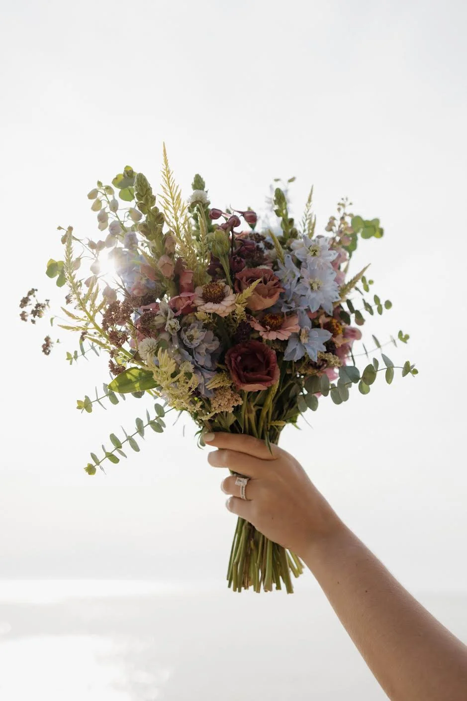 A hand holding a bouquet of assorted flowers against a white background.
