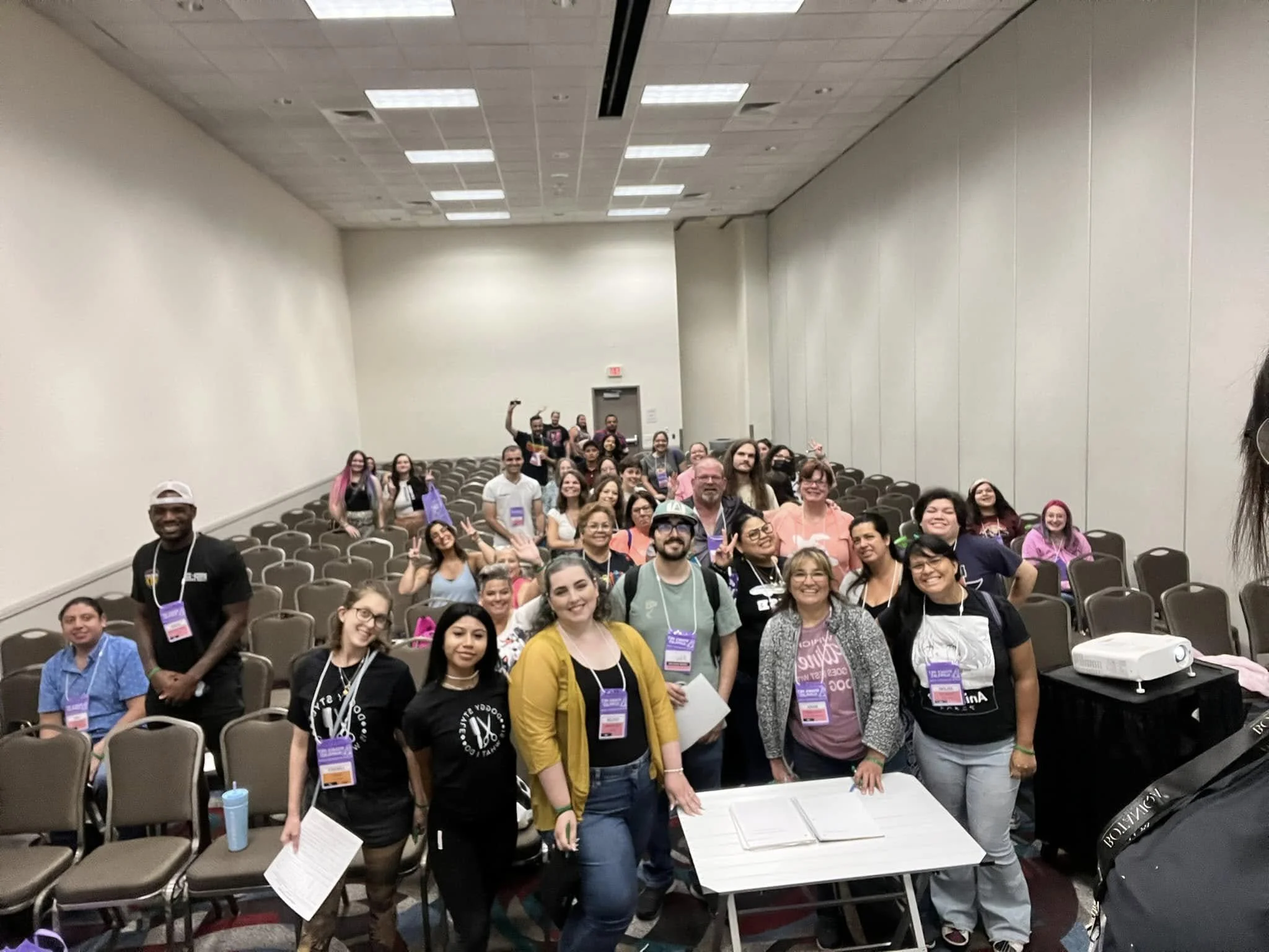 Group of diverse people gathered in a large conference room for a group photo, some standing and smiling at the camera.