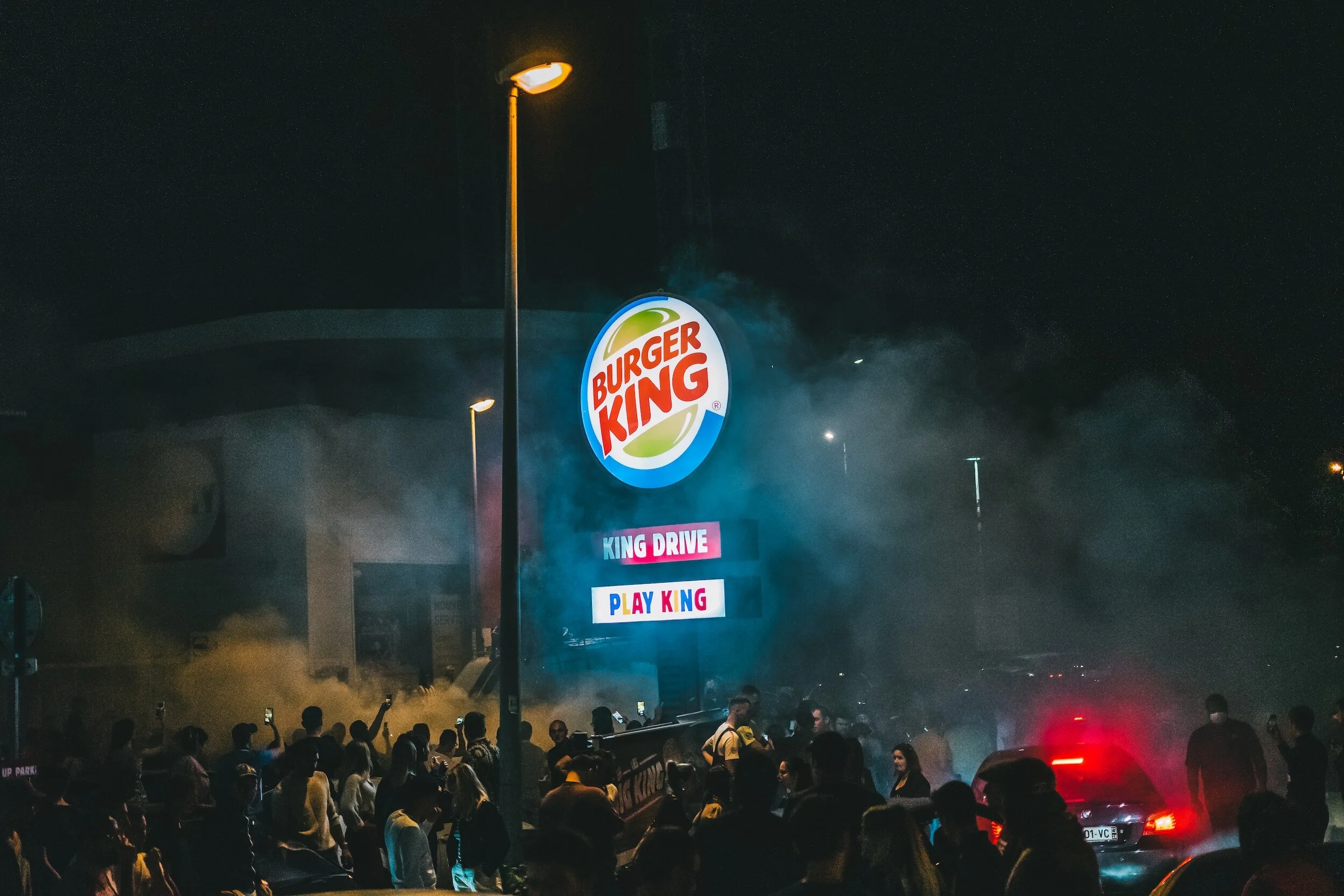 The Burger King Logo in a dark parking lot with smoke and people all around