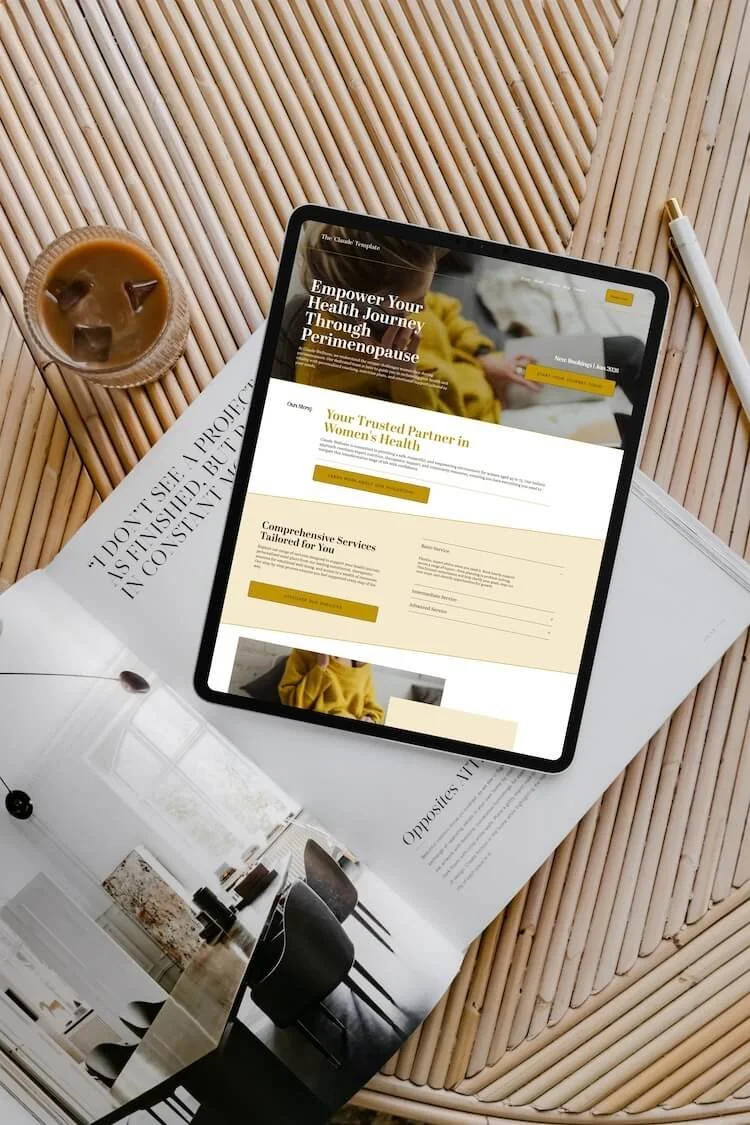 An iPad displaying a website about women's health and menopause, placed on a magazine and a bamboo table next to a glass of iced coffee and a white pen.