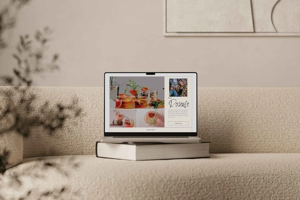 Open laptop displaying a collage of spring-themed photos and text on a closed book on a beige sofa.