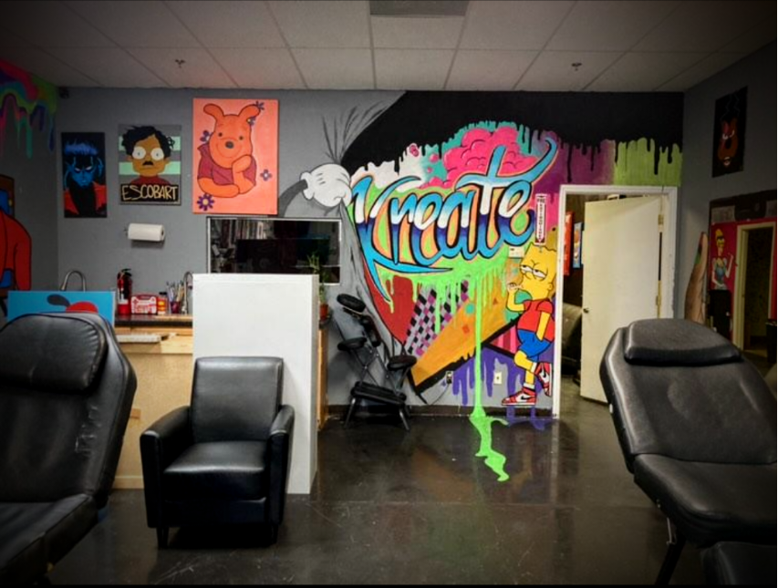 Colorful graffiti art wall featuring the word 'Kreate' with cartoon characters, including Lisa Simpson, and various paint splashes and drips, in a tattoo or art studio setting.