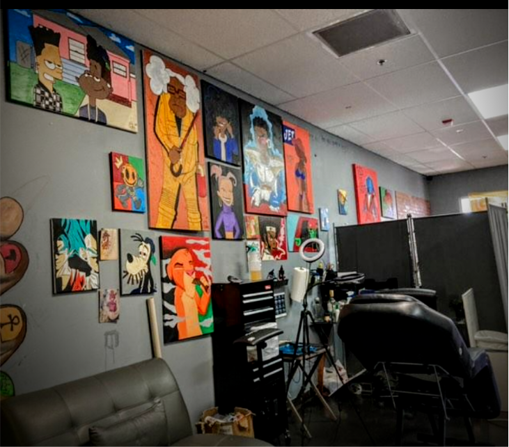 Artistic portraits of cartoon characters and people displayed on the wall of a tattoo or art studio, with tattoo chairs, tools, and equipment visible in the foreground.