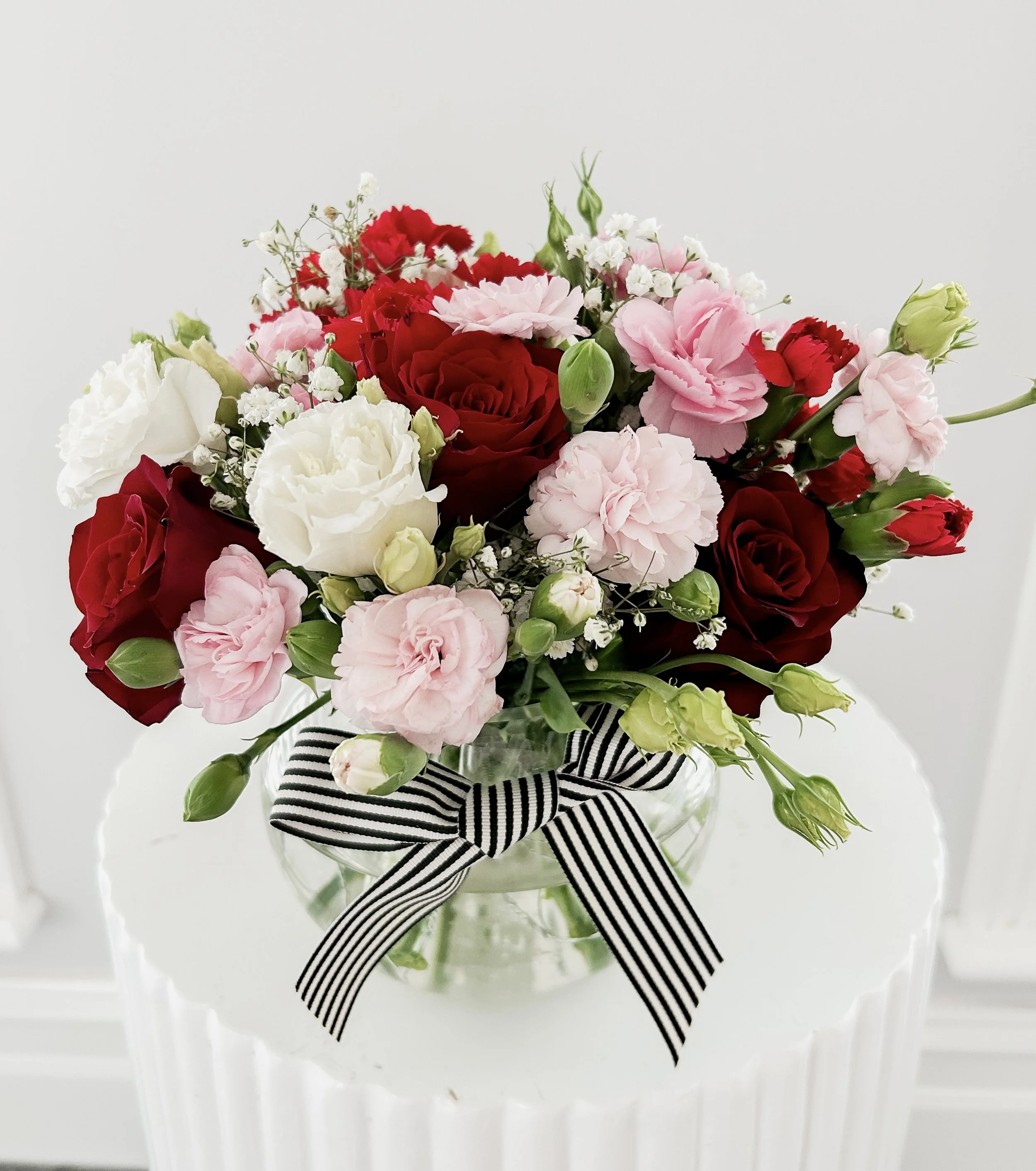 Colorful flower bouquet in a white container with a red ribbon, placed on a white surface