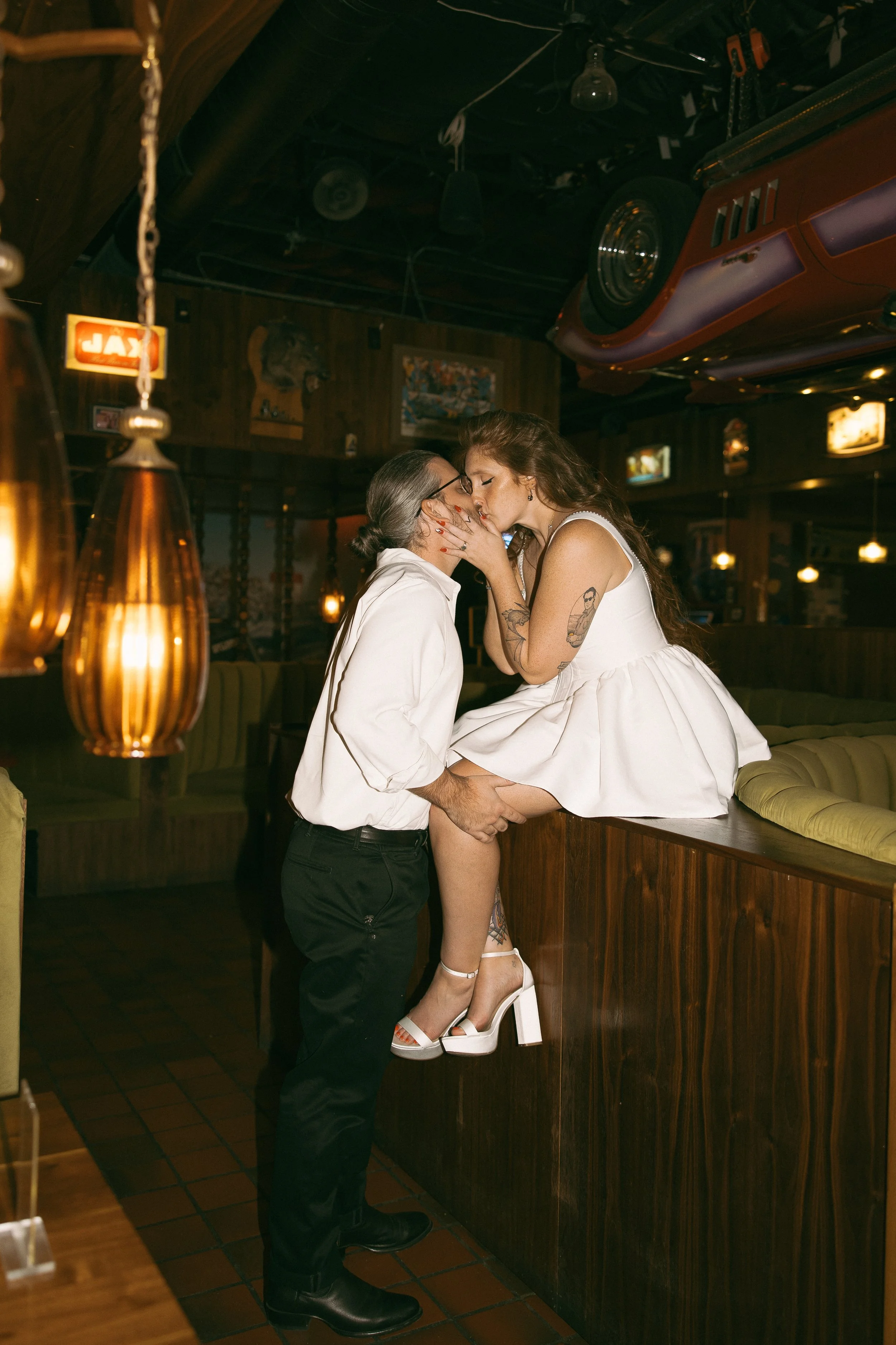 engaged couple posed in Busty's bar in Austin Texas. Bride in short white dress sitting on top of booth kissing groom