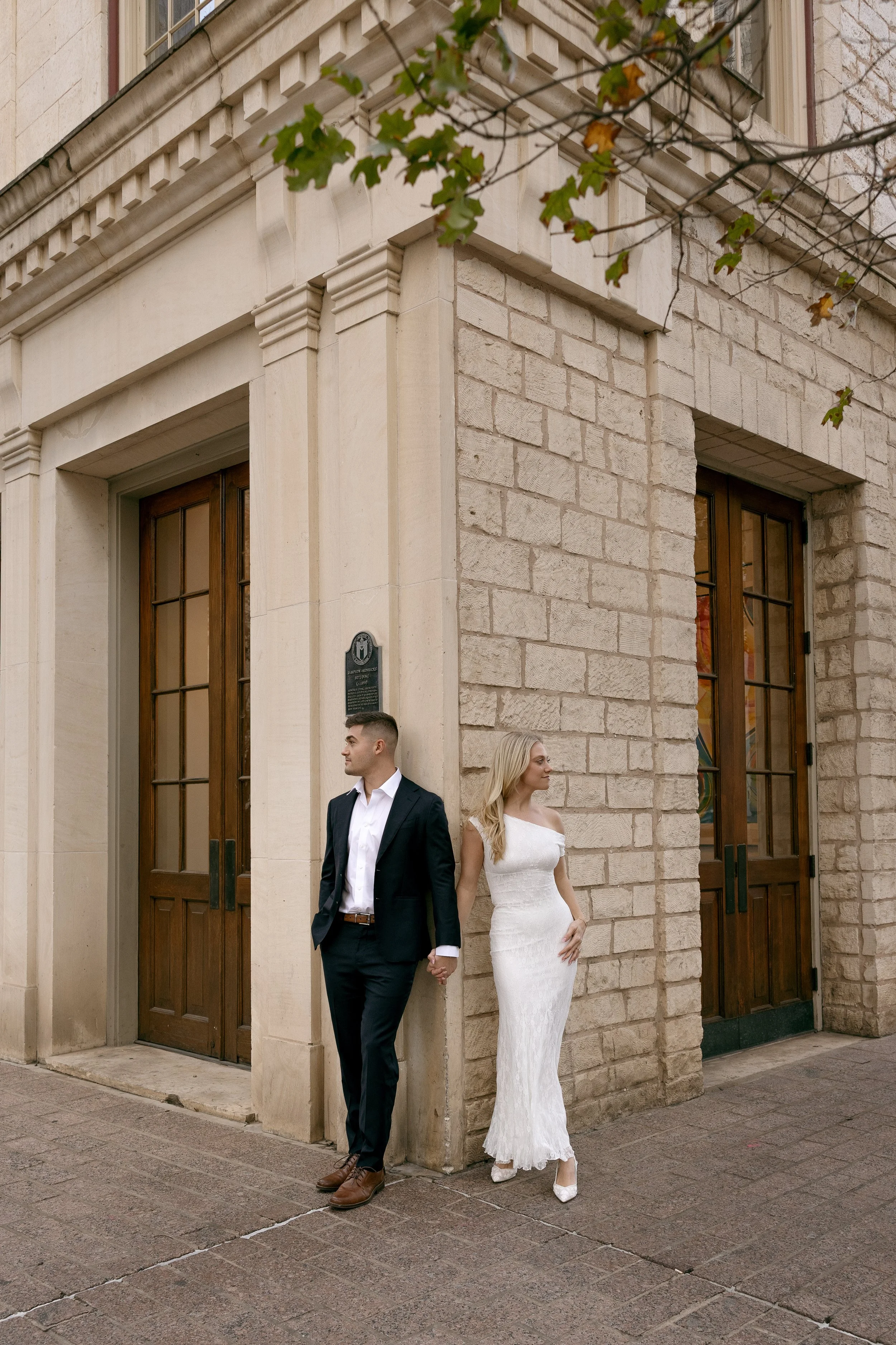 engaged couple in downtown austin posed against a building. groom in suit and bride in white formal dress both looking off