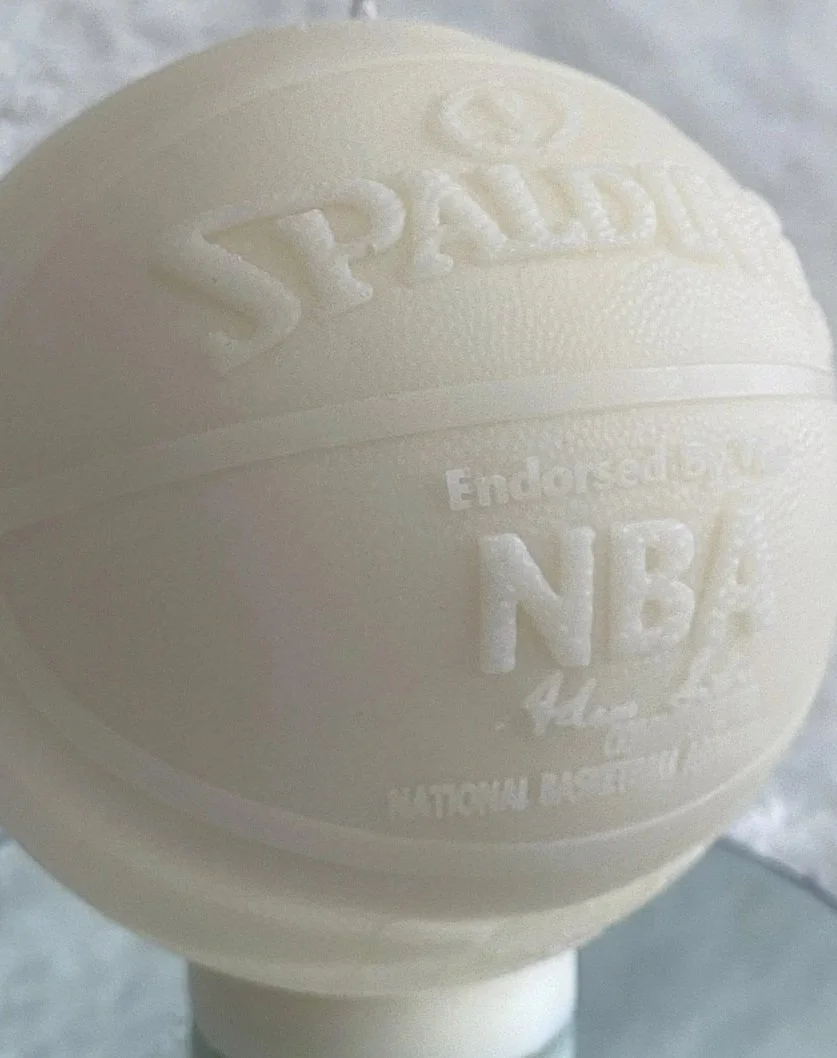 Close-up of a white, textured Rugby brand tennis ball with embossed text and logo.
