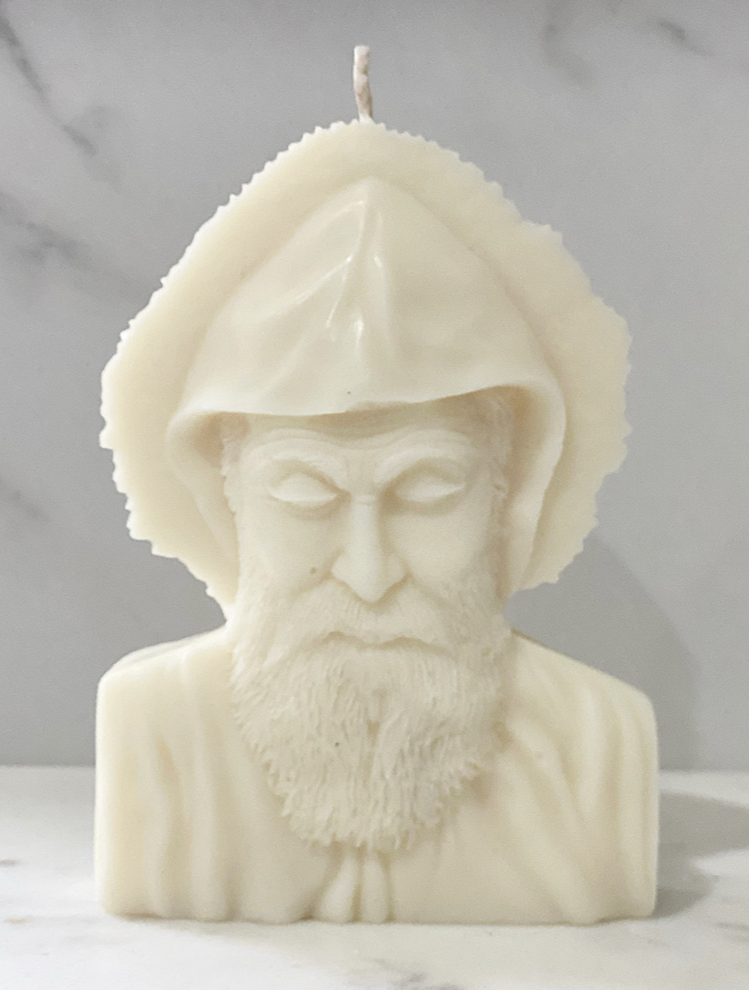 A white candle shaped like a bust of an elderly man with a beard and a bonnet, with a small flame at the top.