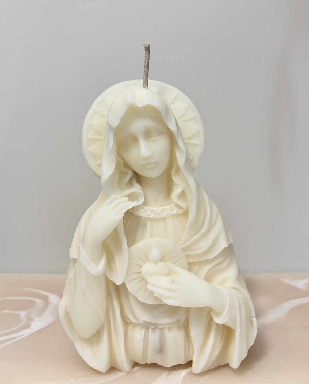 Cream-colored religious sculpture depicting Jesus with a halo, holding a sacred heart, with a candle wick on top.