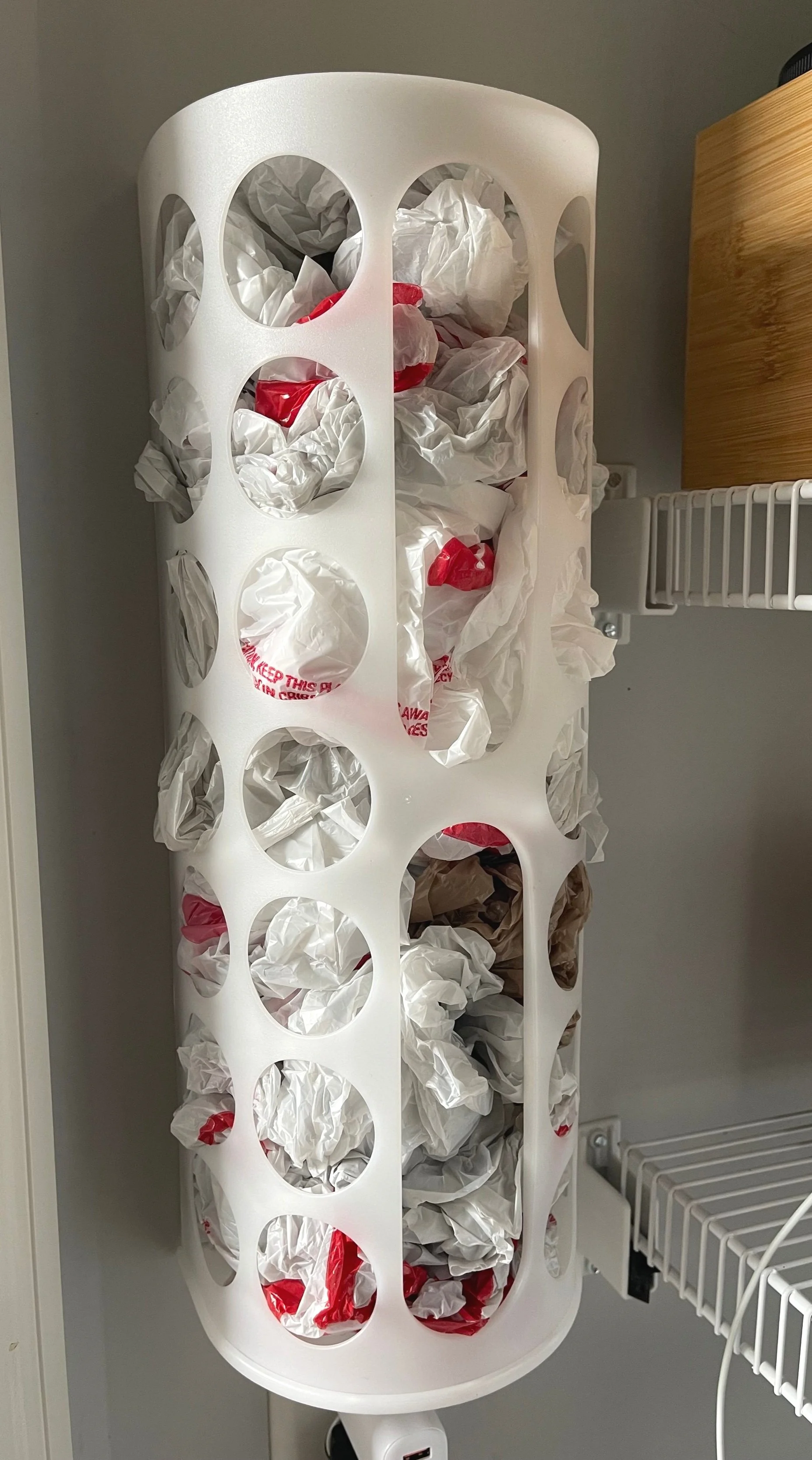 IKEA VARIERA plastic bag dispenser mounted inside a pantry to keep grocery bags neatly contained and easy to access.