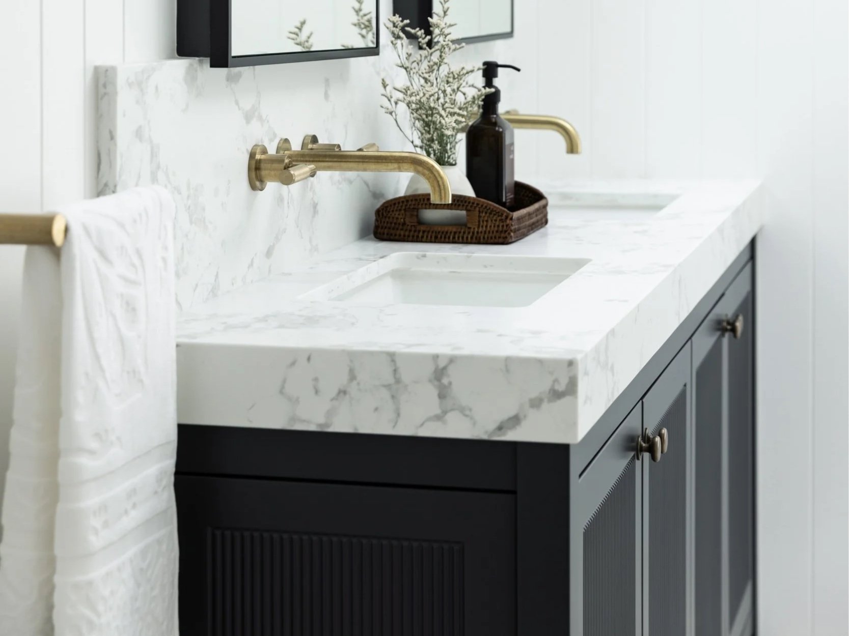 Elegant residential bathroom with a white marble vanity, brass tapware, statement wall lighting and a framed mirror.