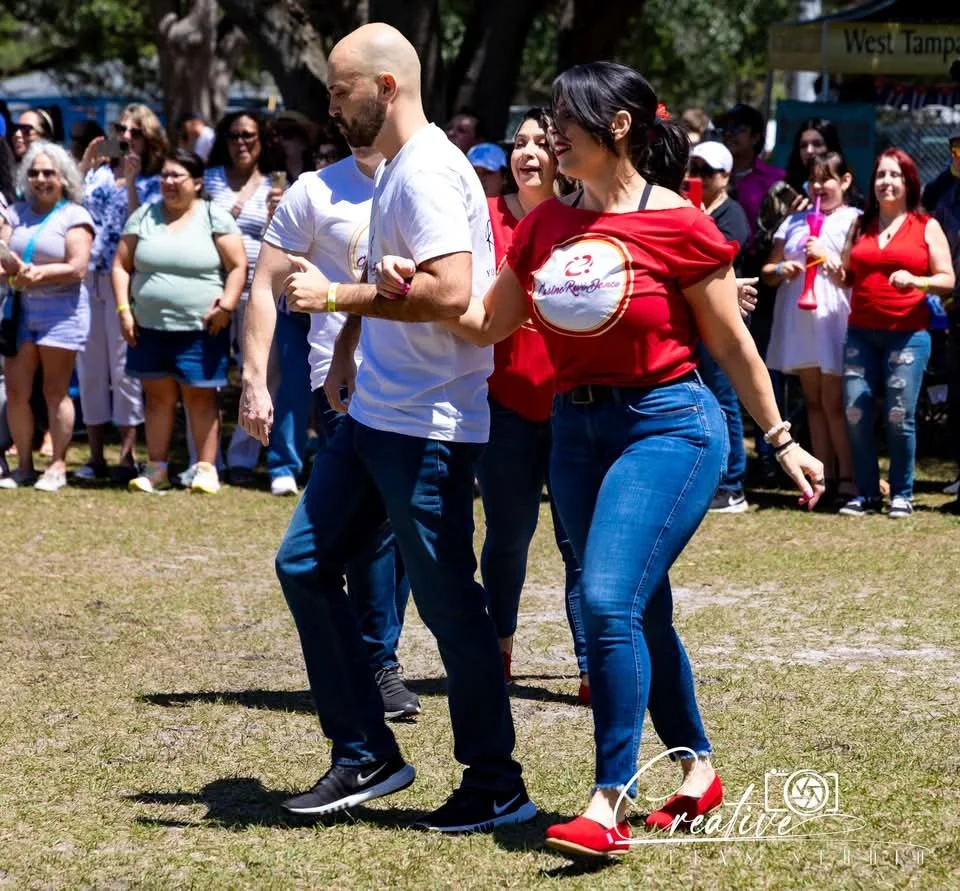 Group of people dancing outdoors at an event, with a crowd watching in the background.