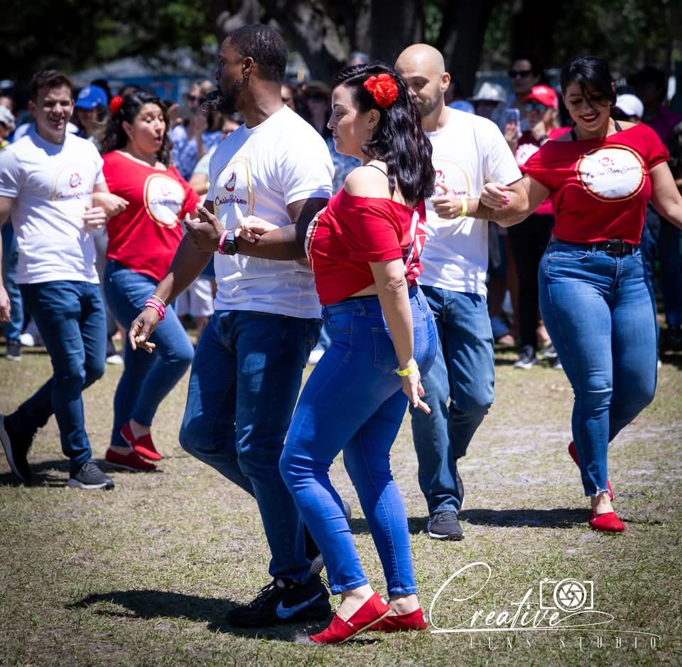 Group of people dancing outdoors in a park, wearing matching red and white outfits.
