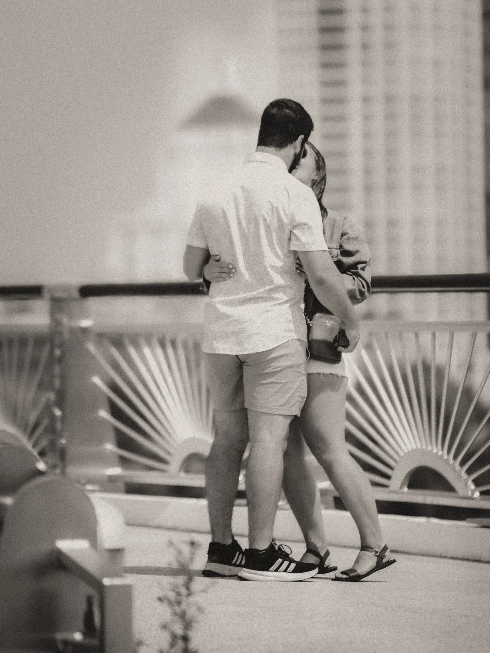 A young couple hugging and kissing on a rooftop, with city buildings in the background, in black and white.
