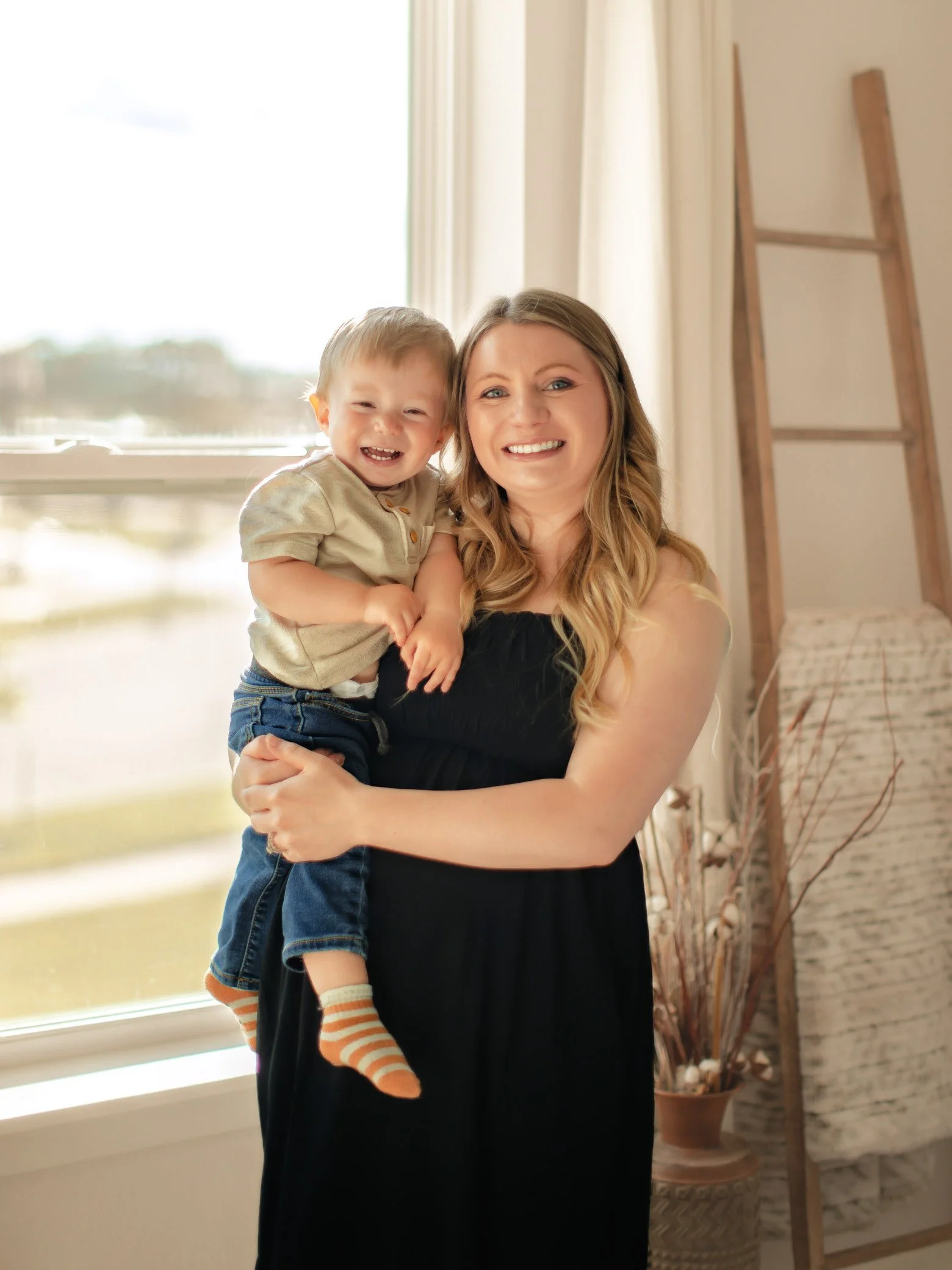 A woman holding a young boy indoors near a window, smiling and laughing.
